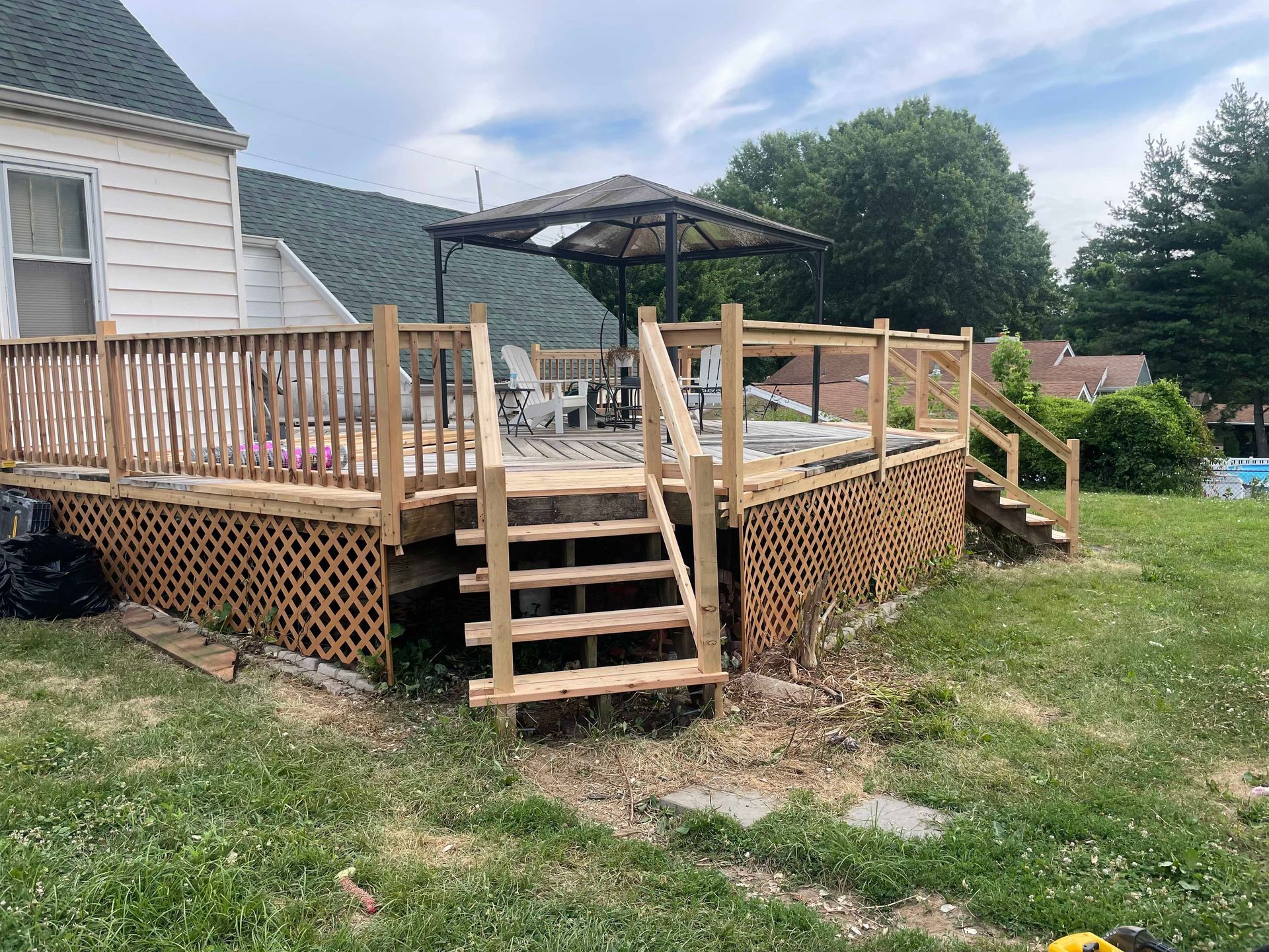 Wooden deck with stairs, lattice skirting, and gazebo, next to a house on a grassy lawn.