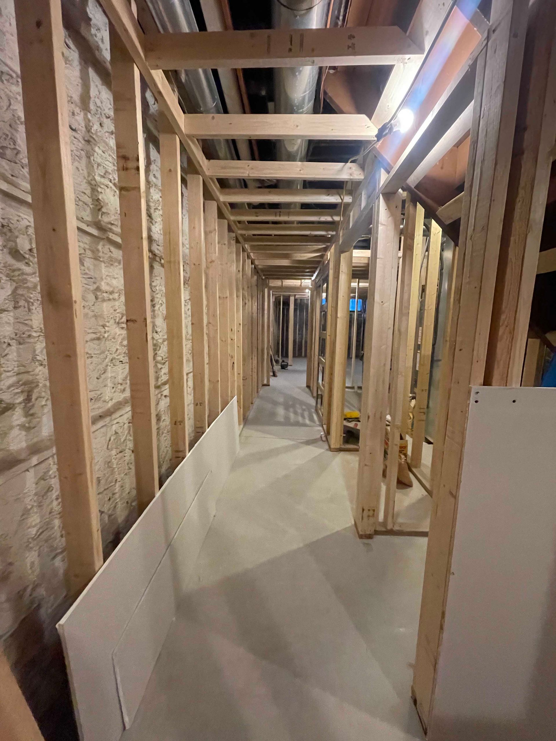 Interior view of a narrow unfinished hallway with wooden framing and exposed pipes overhead.