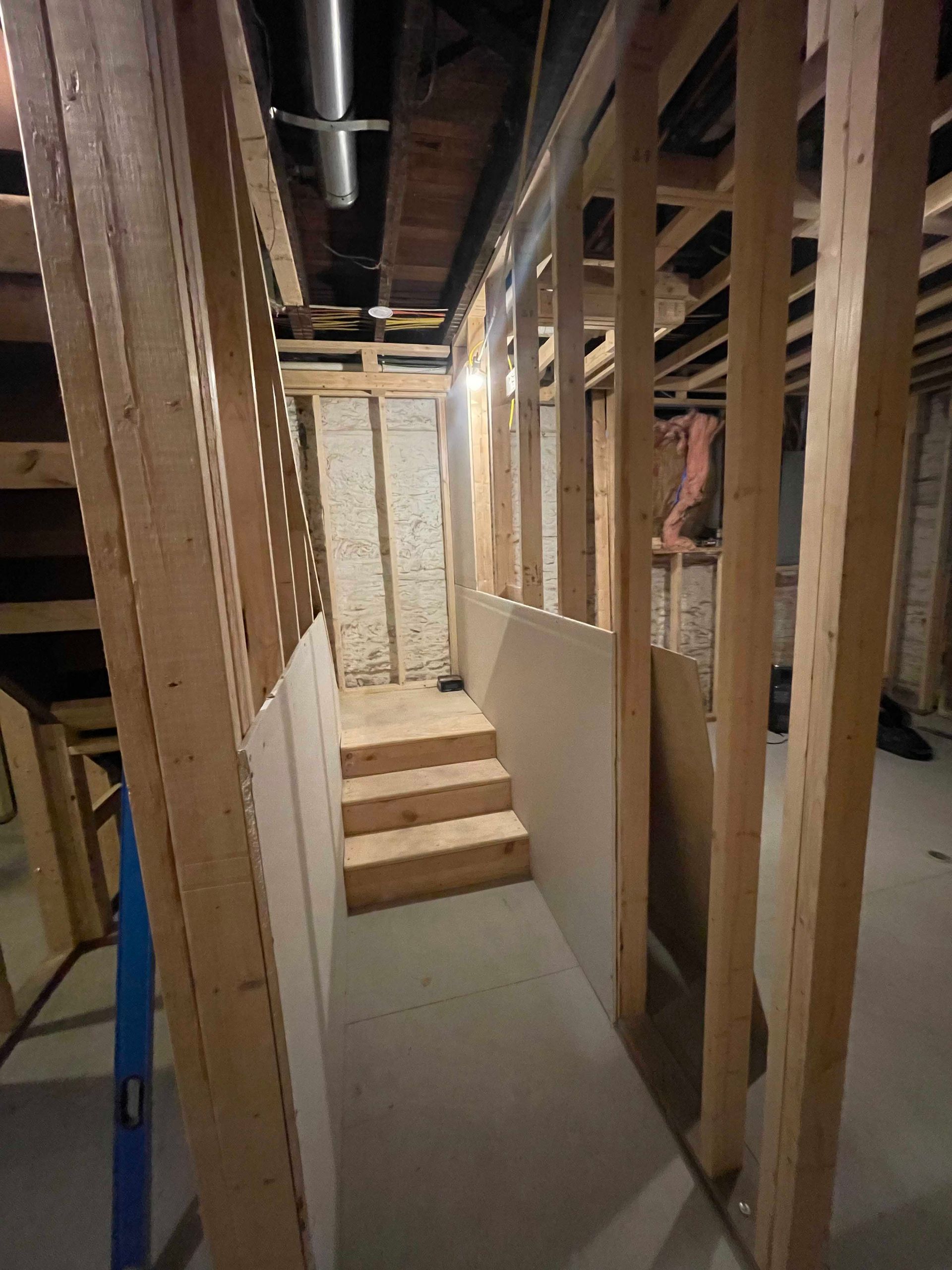Framed wooden stairs leading down. Basement construction with exposed studs, drywall, and concrete floor.