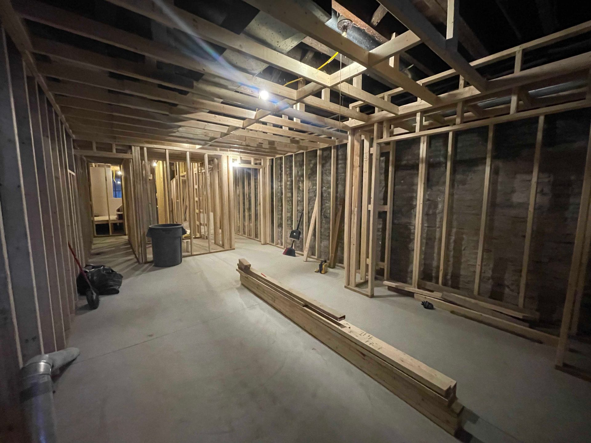 Interior view of a room under construction with exposed wooden framing for walls and ceiling, concrete floor.