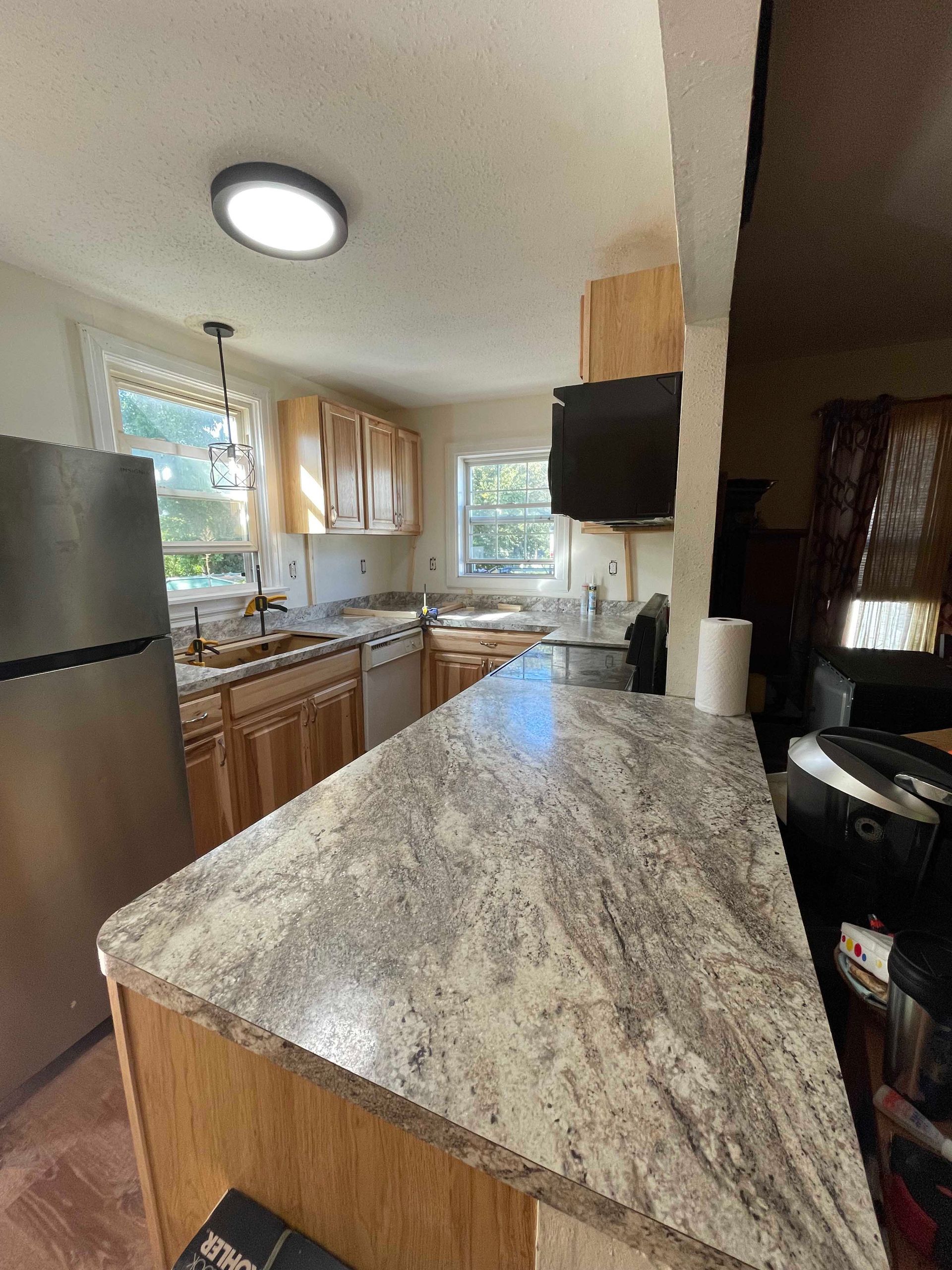 Kitchen with wood cabinets, granite countertop, stainless steel refrigerator, and a recessed ceiling light.