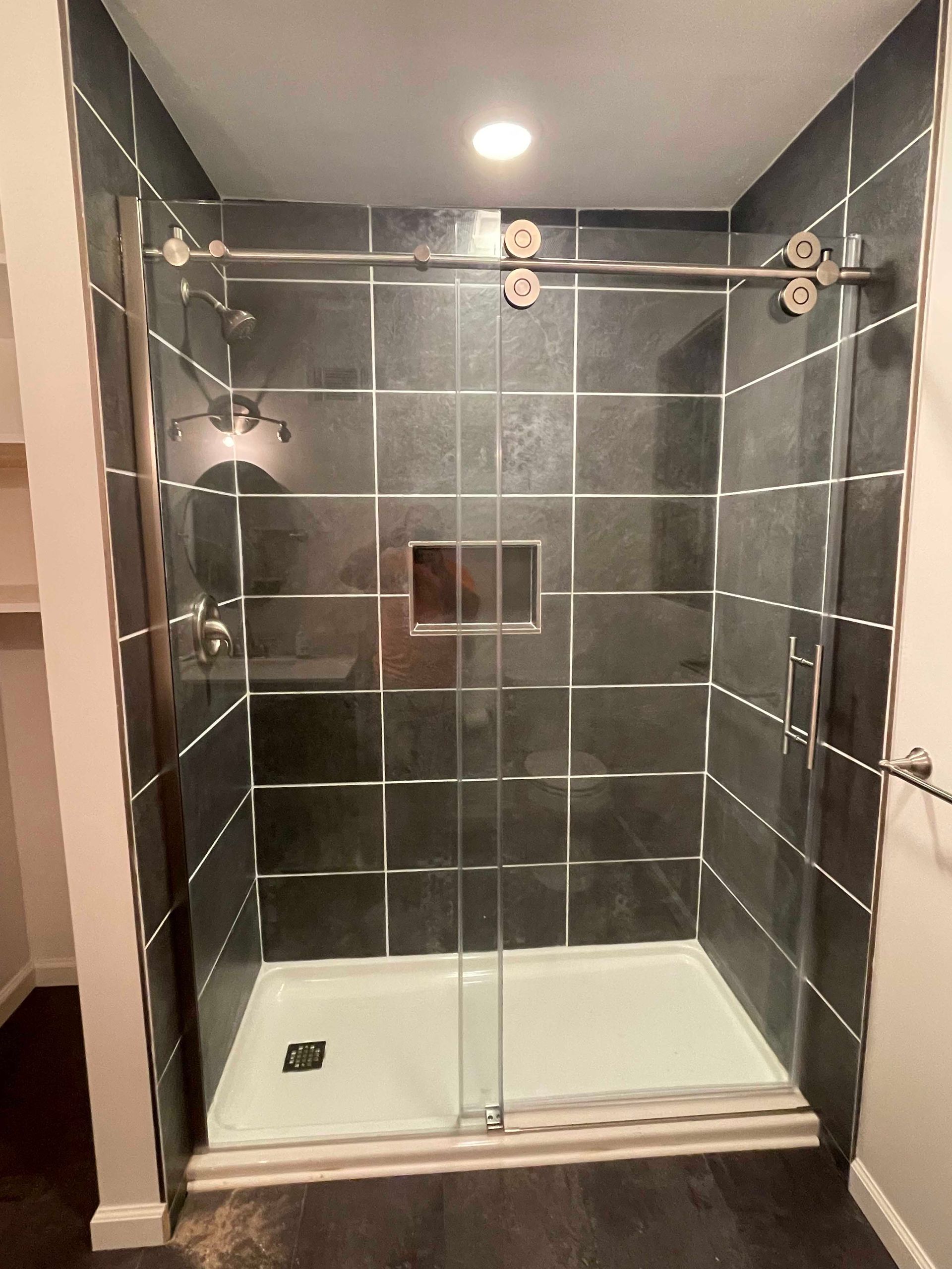 Modern shower with dark gray tile and sliding glass doors. White shower base and silver hardware.