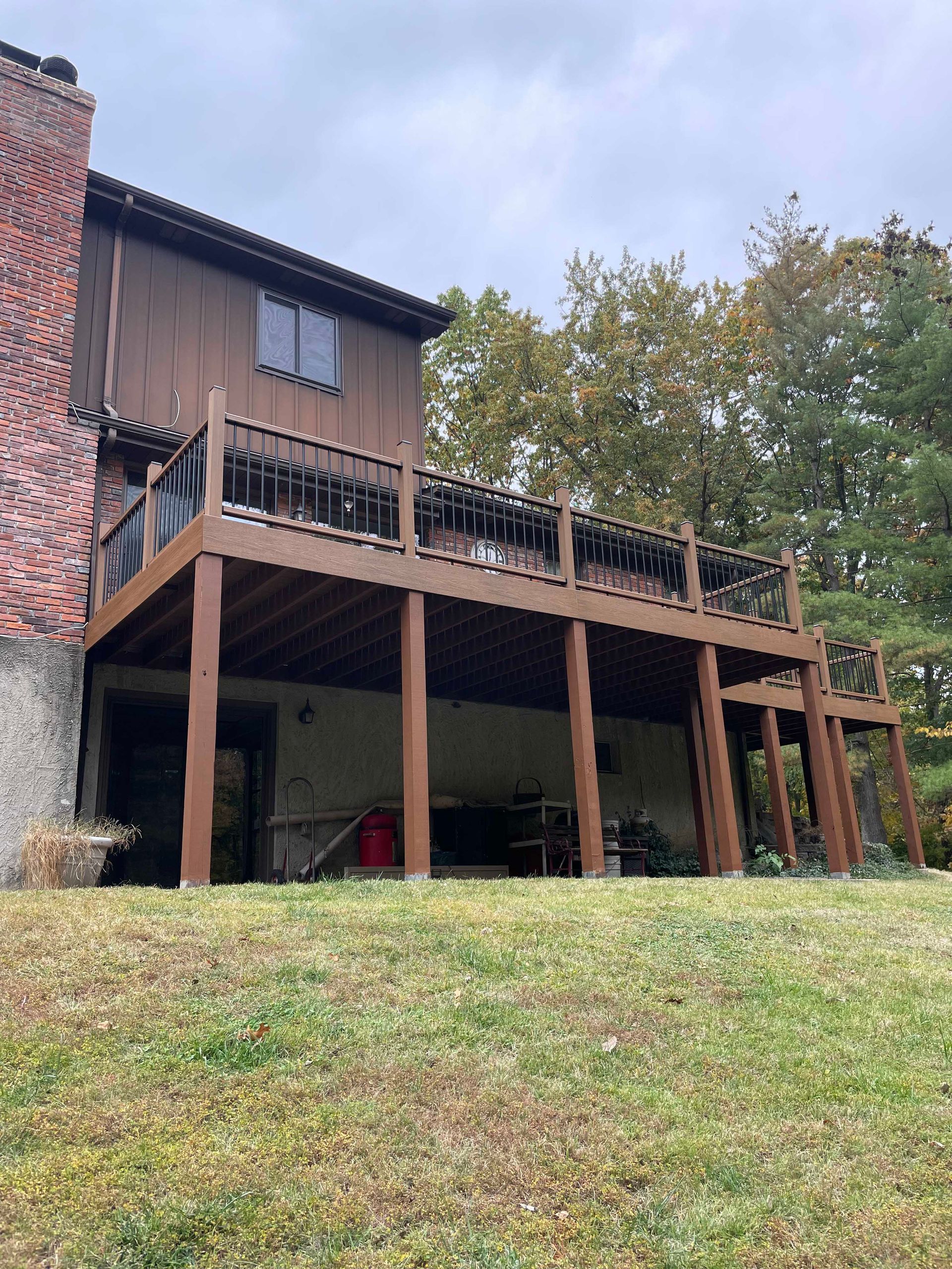 Brown wooden deck extending from a two-story house with a brick chimney, overlooking a grassy yard.