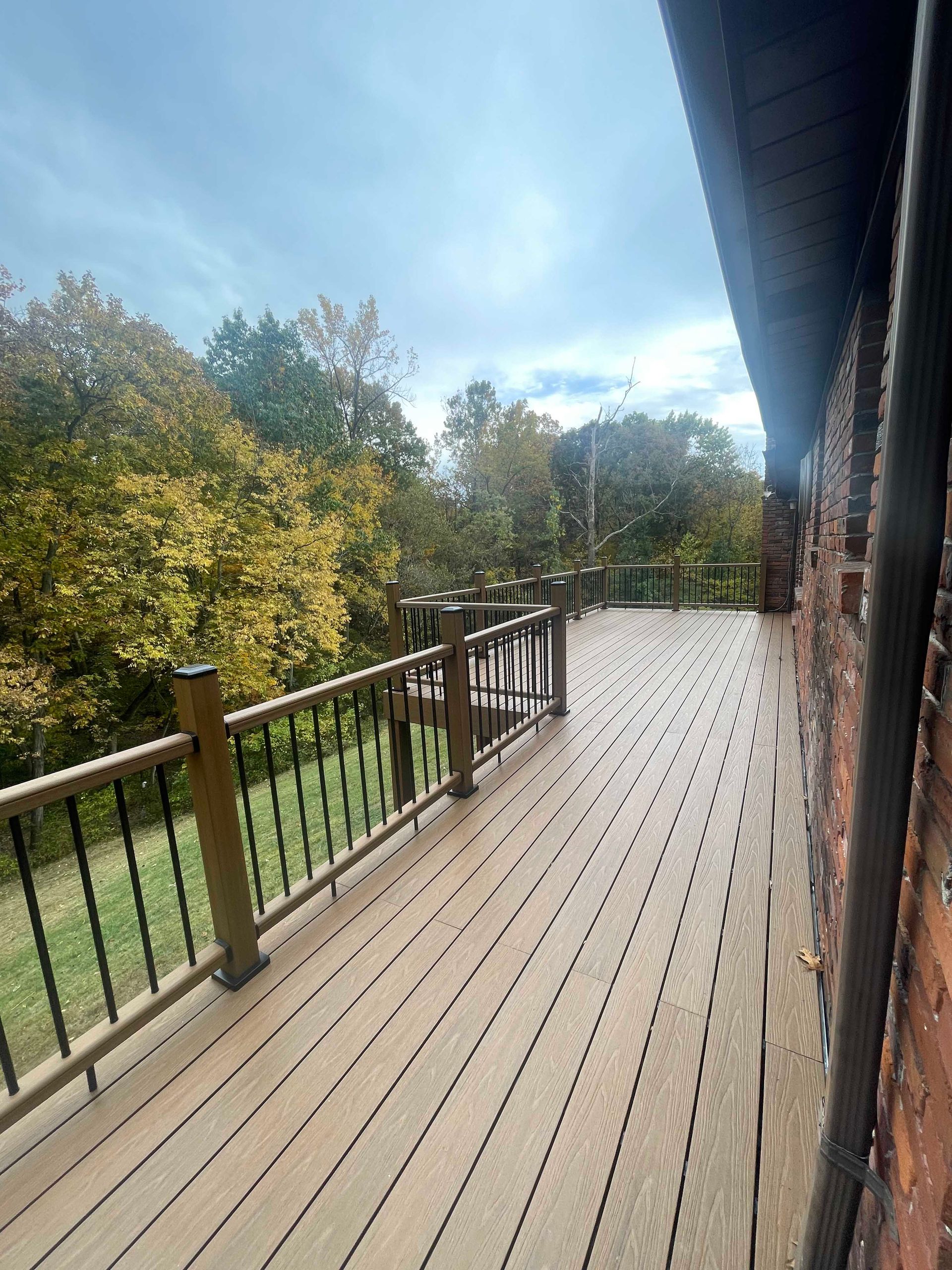 Deck overlooking trees and foliage on a cloudy day, beside a brick building.