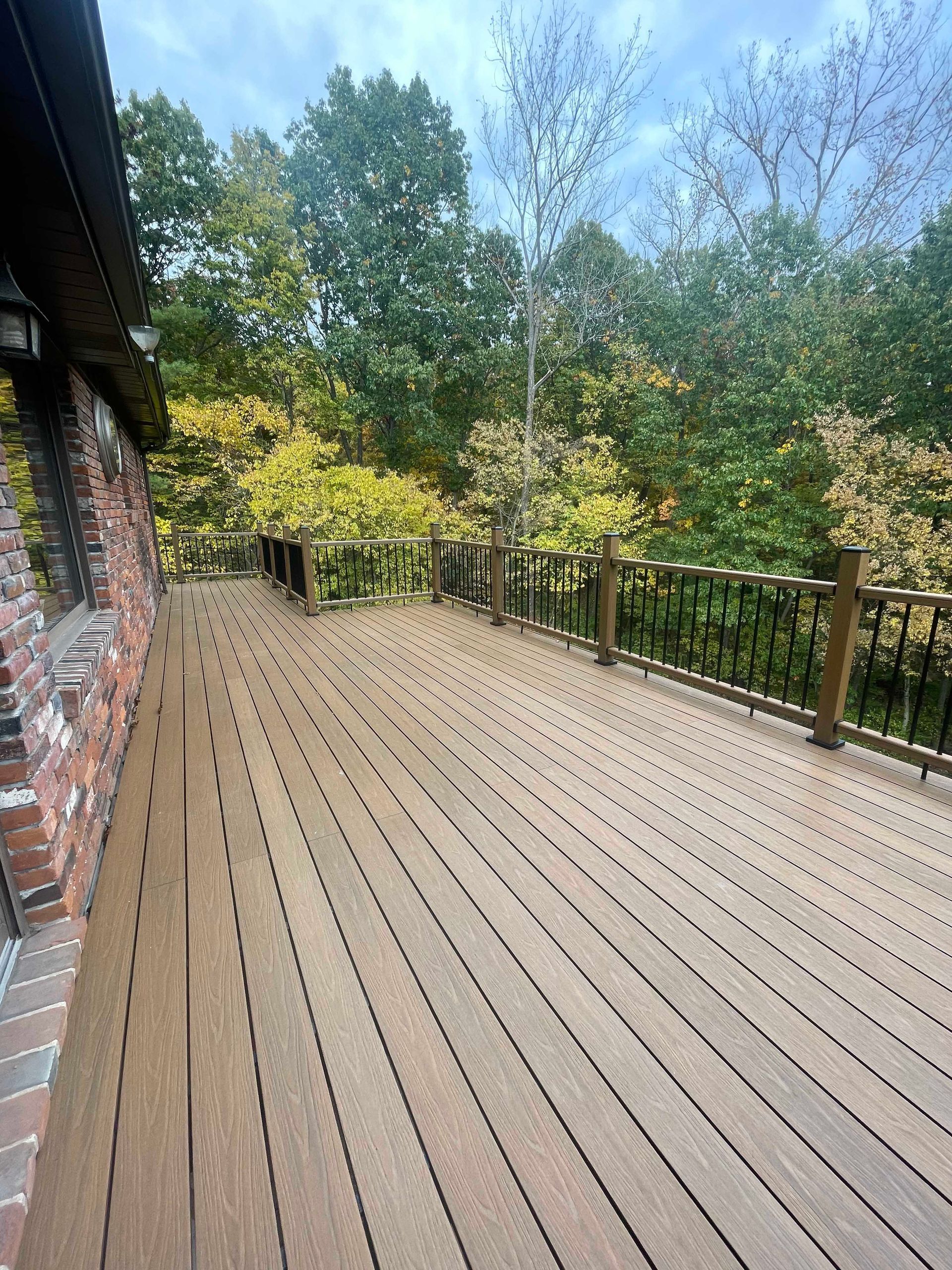 Wooden deck with black railing and trees in background.