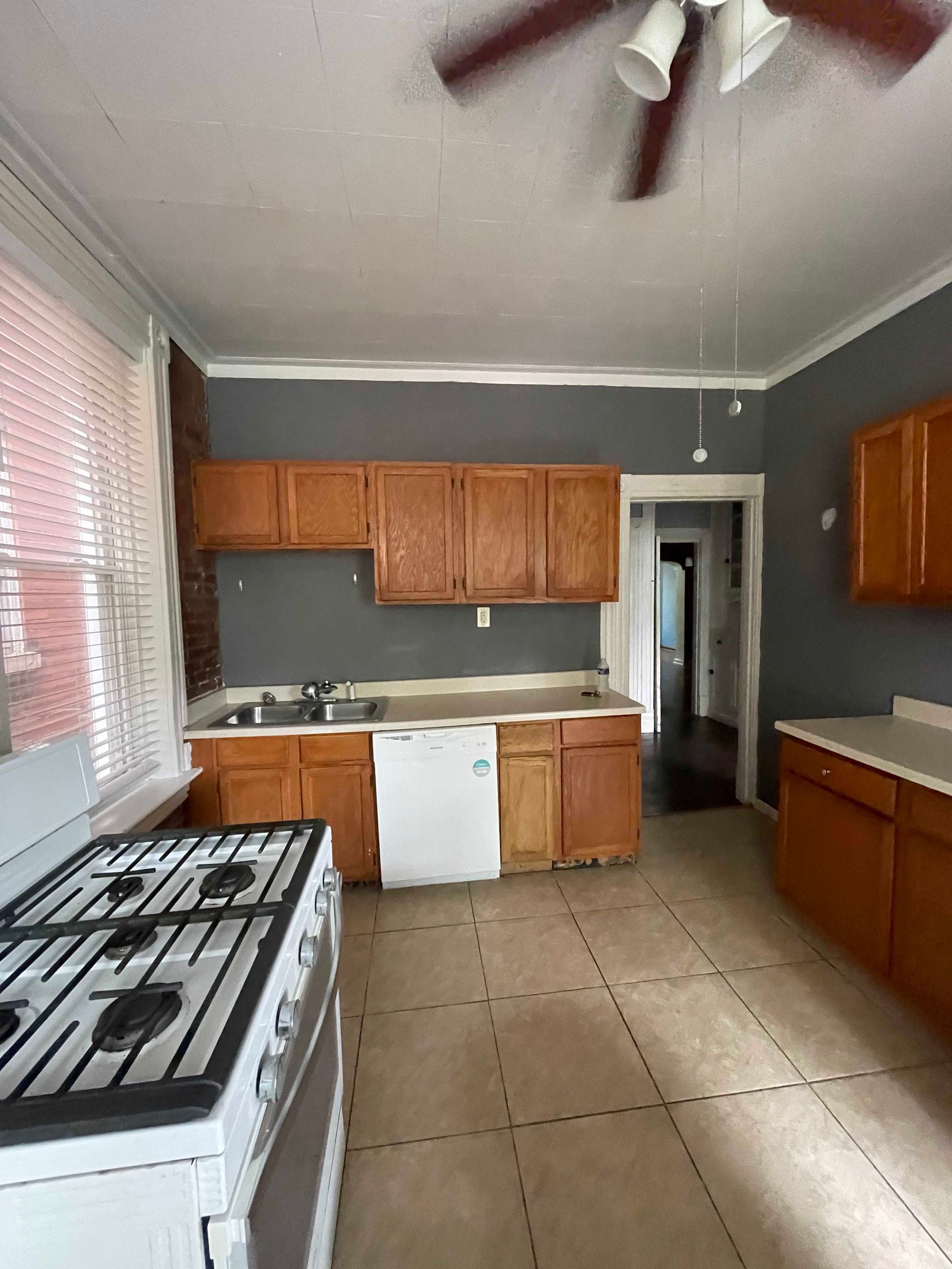 Kitchen with wooden cabinets, gray walls, white appliances, and a tiled floor.