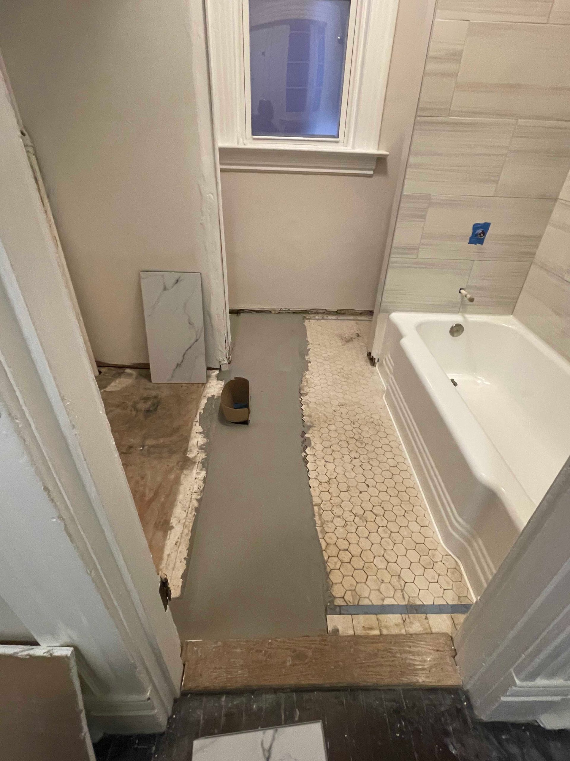 Bathroom renovation: half-tiled wall, bathtub, floor prep, doorway. White, gray, and brown.