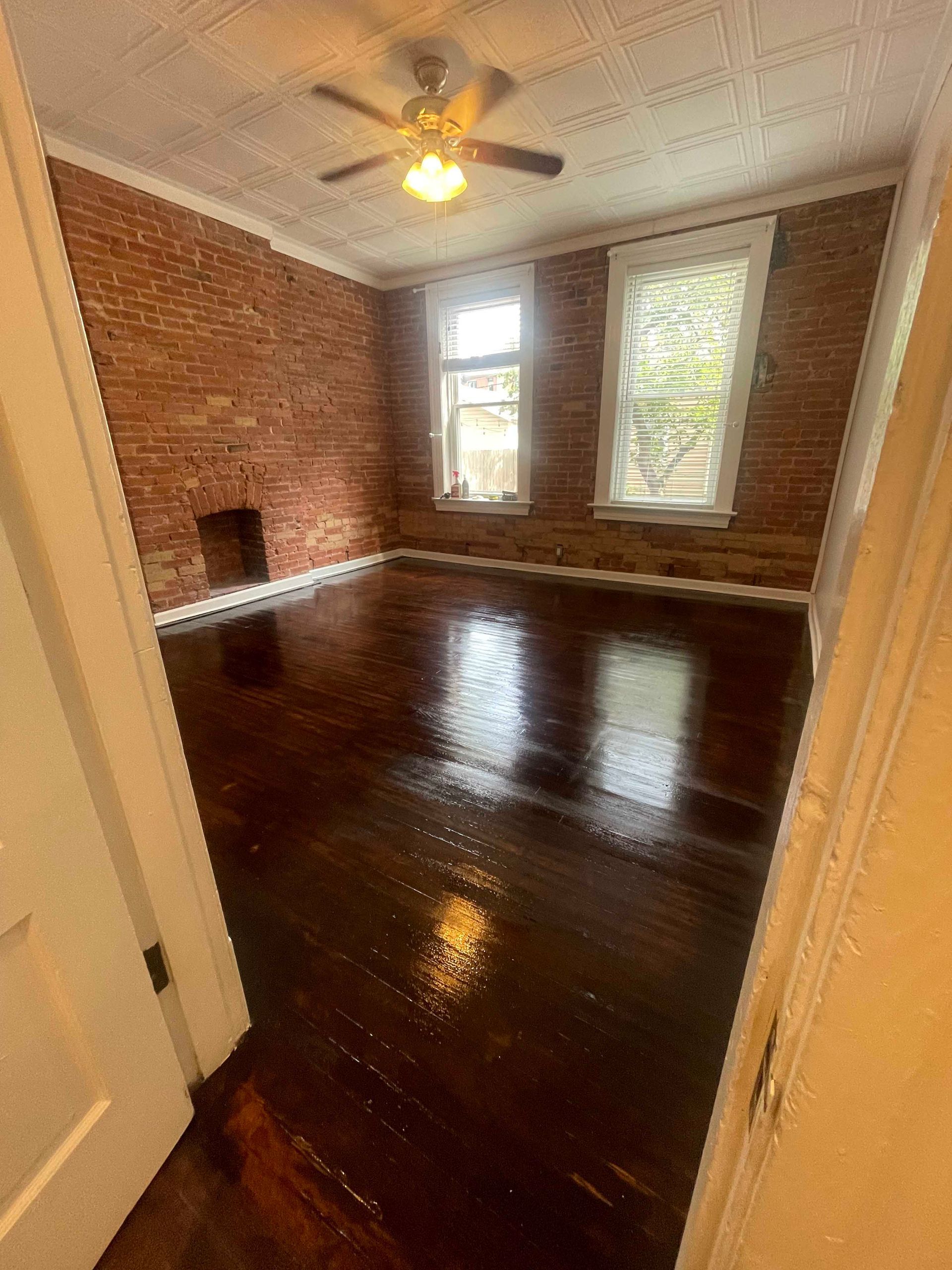 Empty room with exposed brick walls, dark wood floors, and two windows.