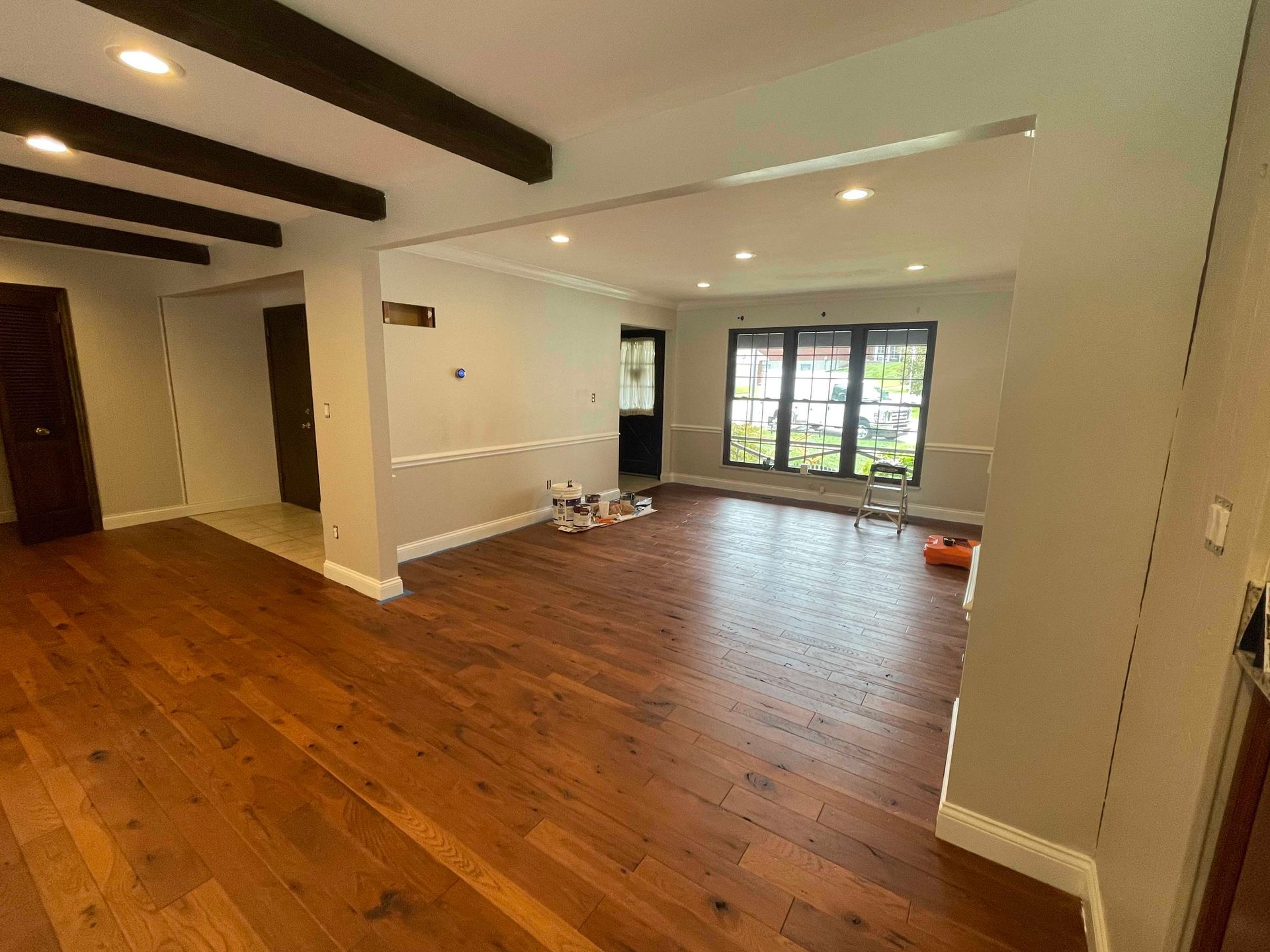 Empty living room with wood floors, exposed beams, and dark trim.