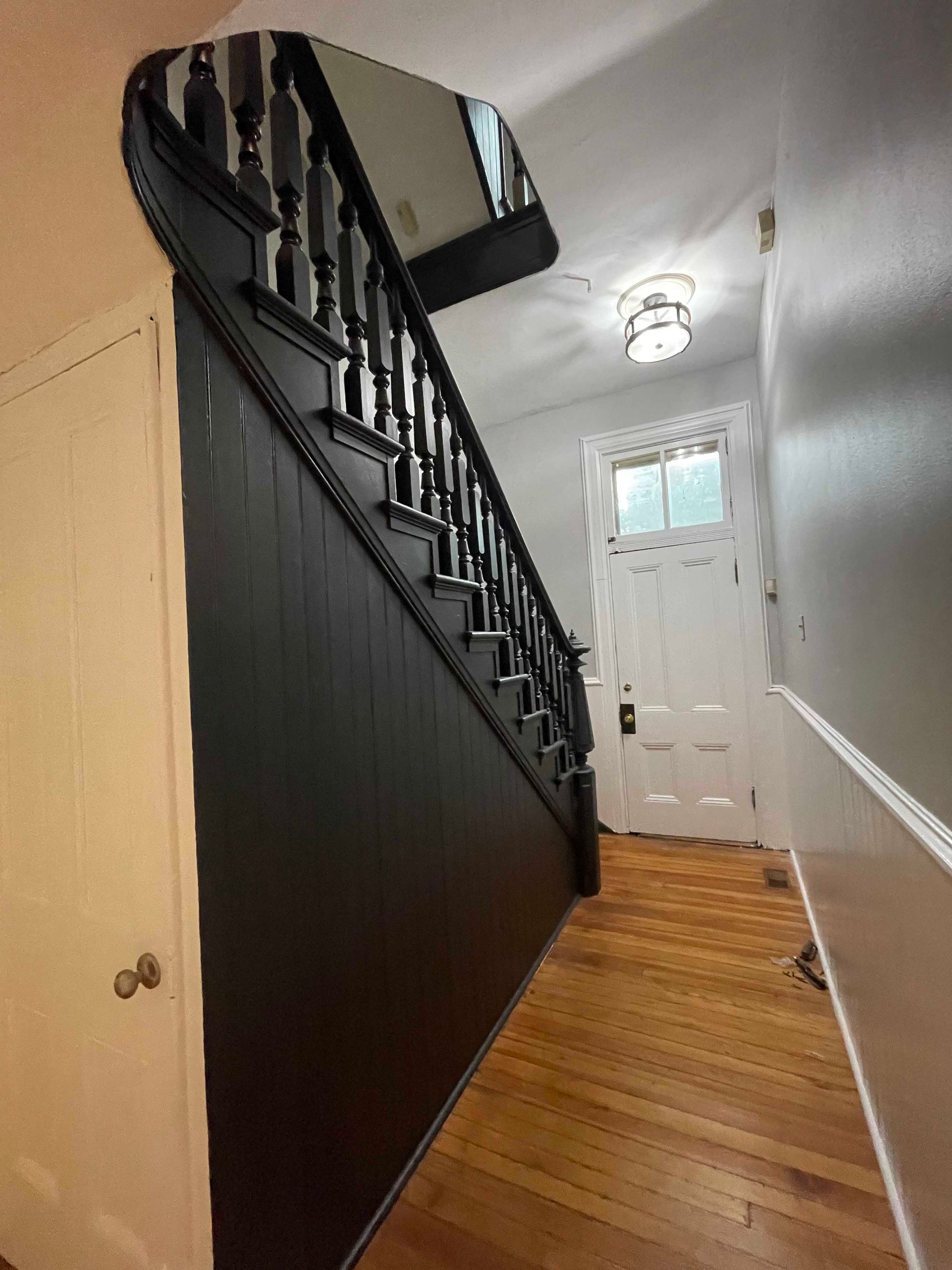 Black painted staircase with a wooden railing and a white door at the end of the hallway.