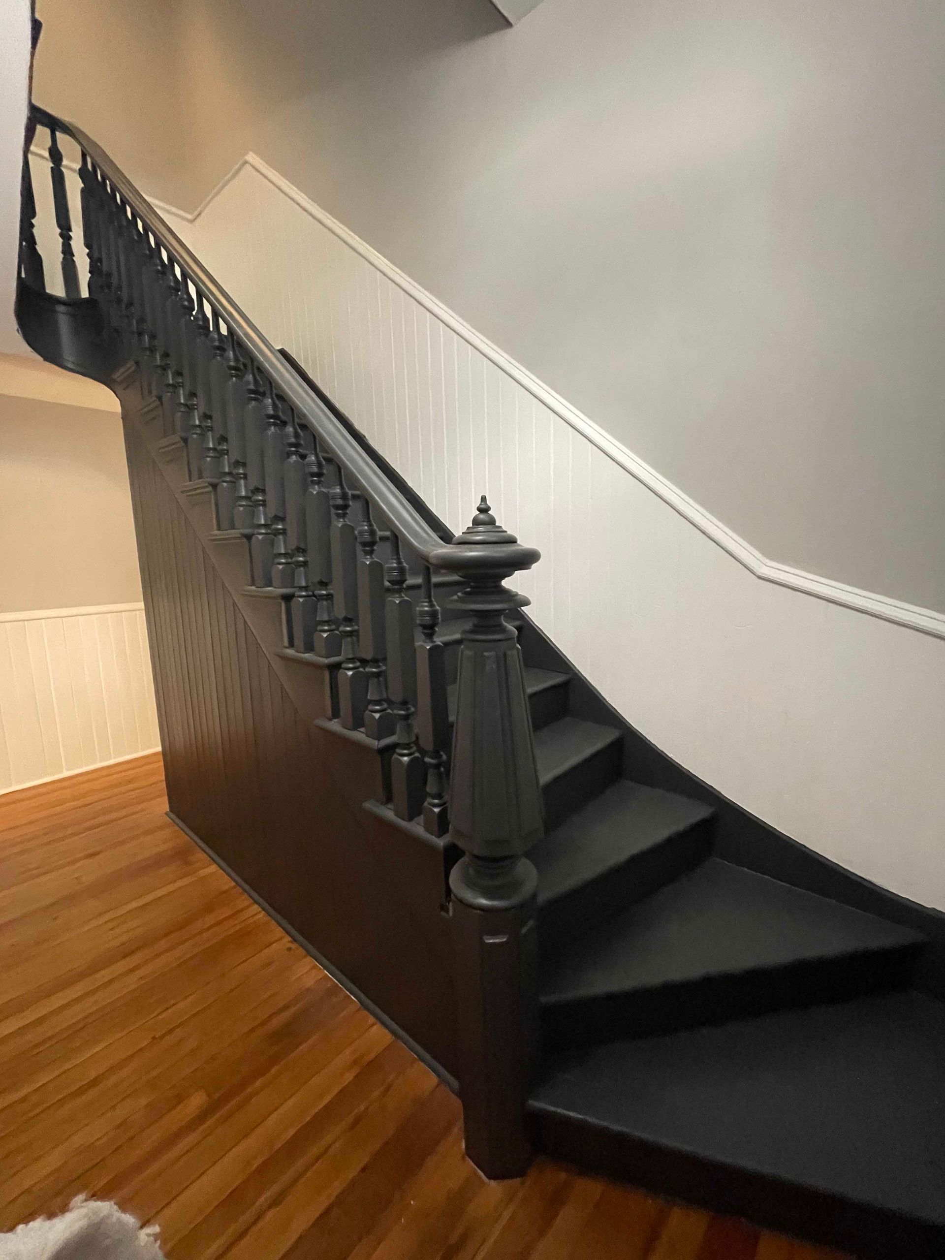Black painted staircase with white wall and wooden floor.