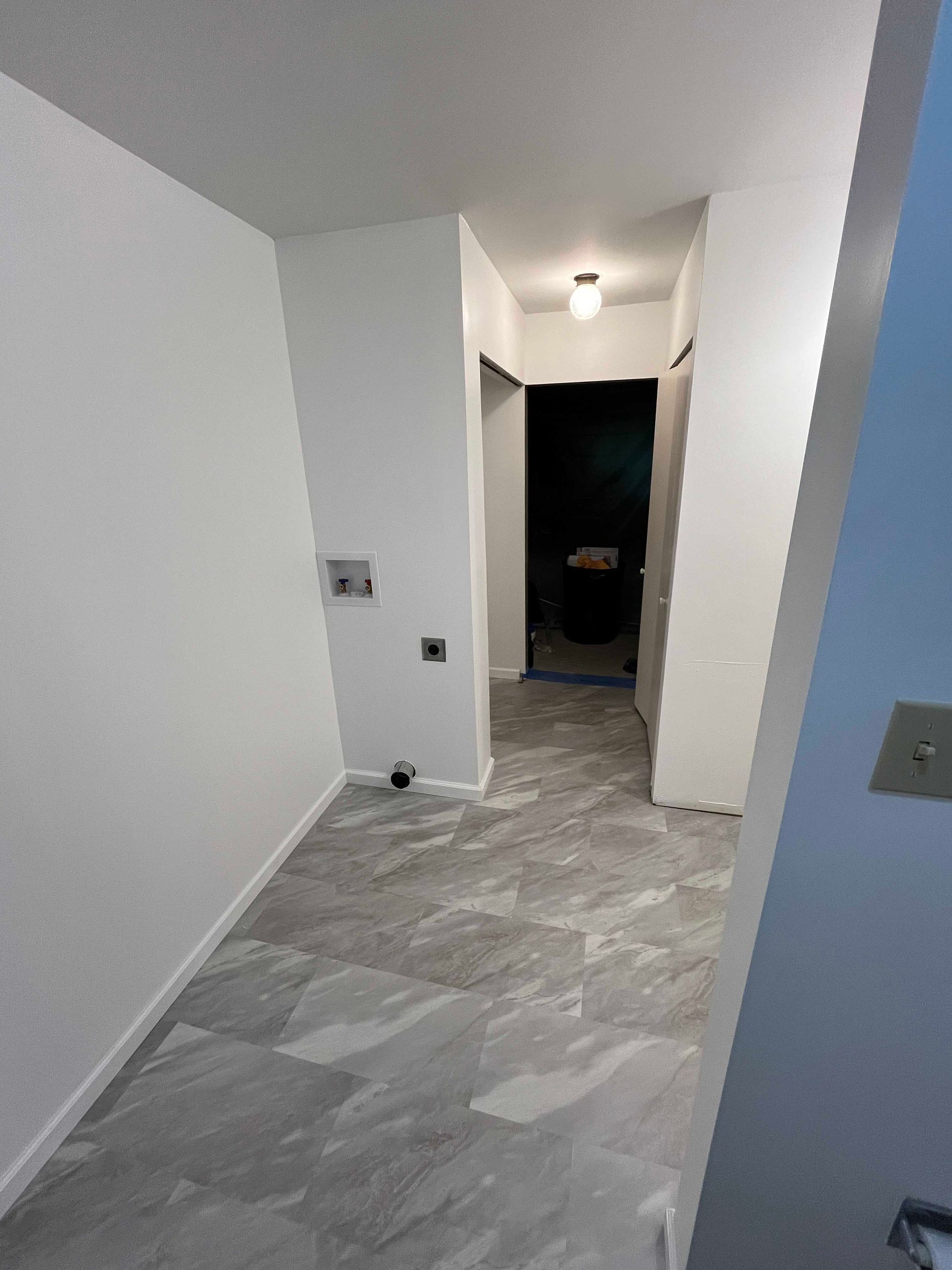 Empty hallway with gray tiled floor and white walls, leading to a dark doorway.