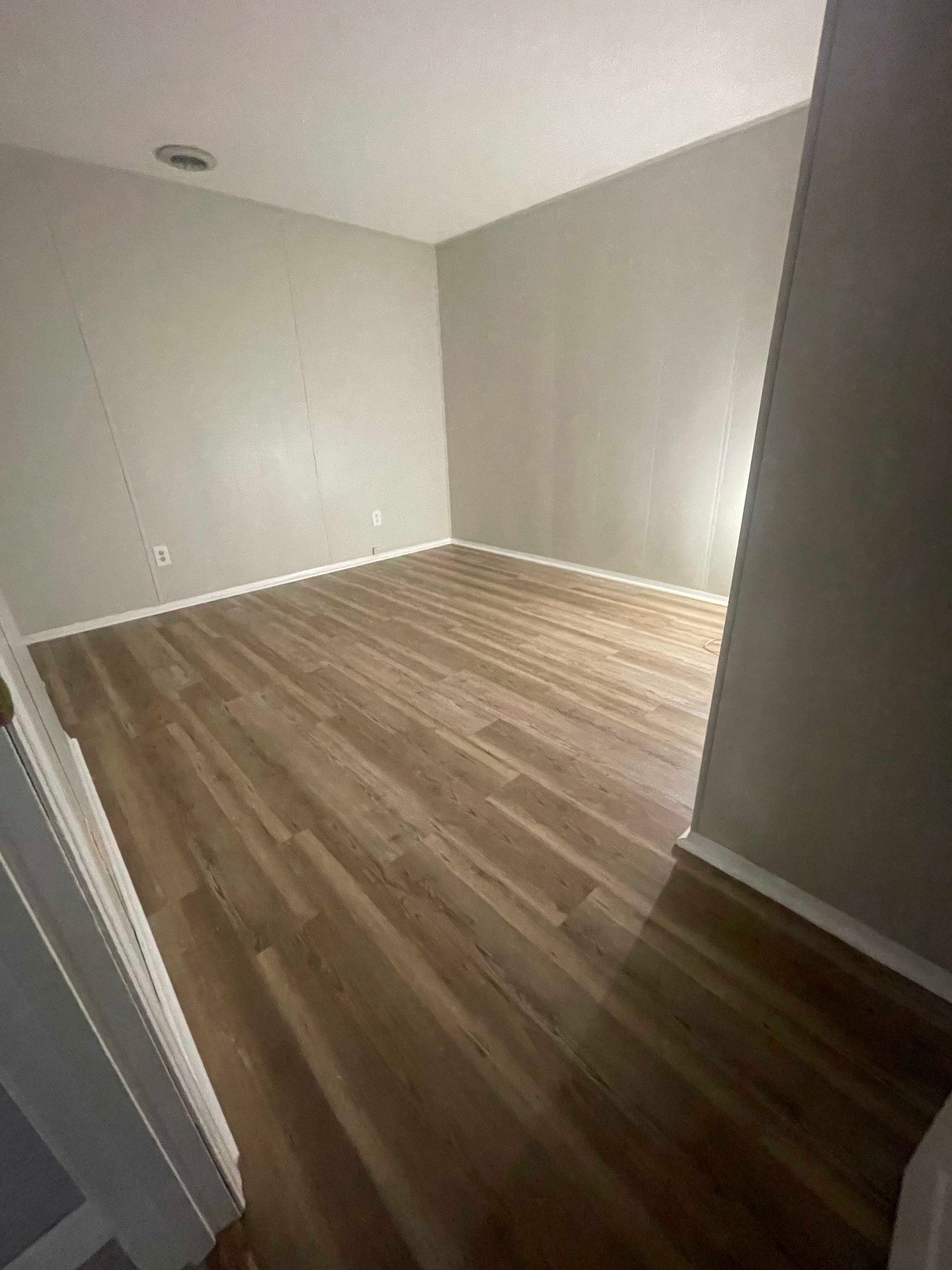 Empty room with wood-look flooring and gray walls. Light enters from a window.