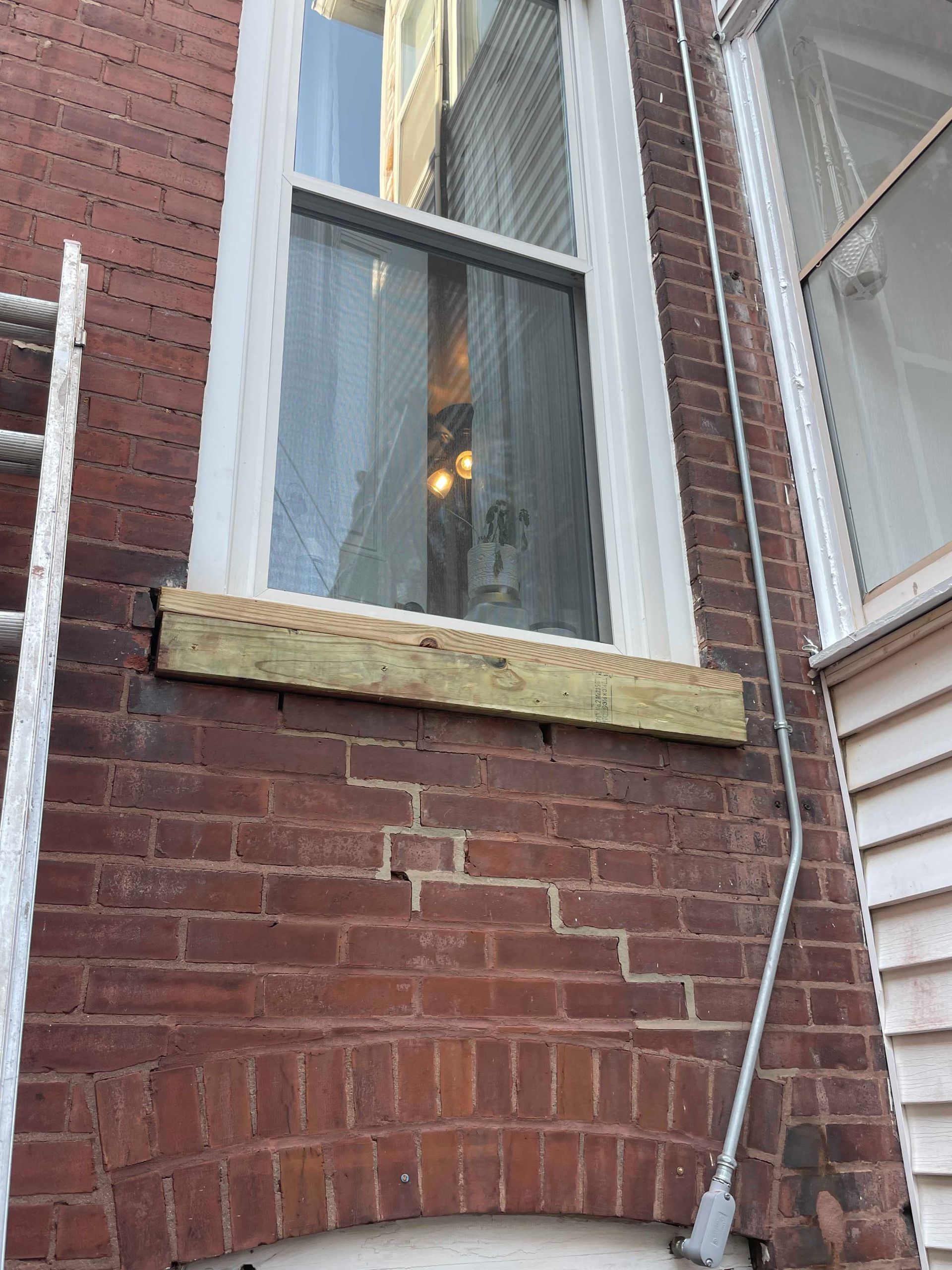 Exterior view of a brick building with a window and a wooden board attached below it.