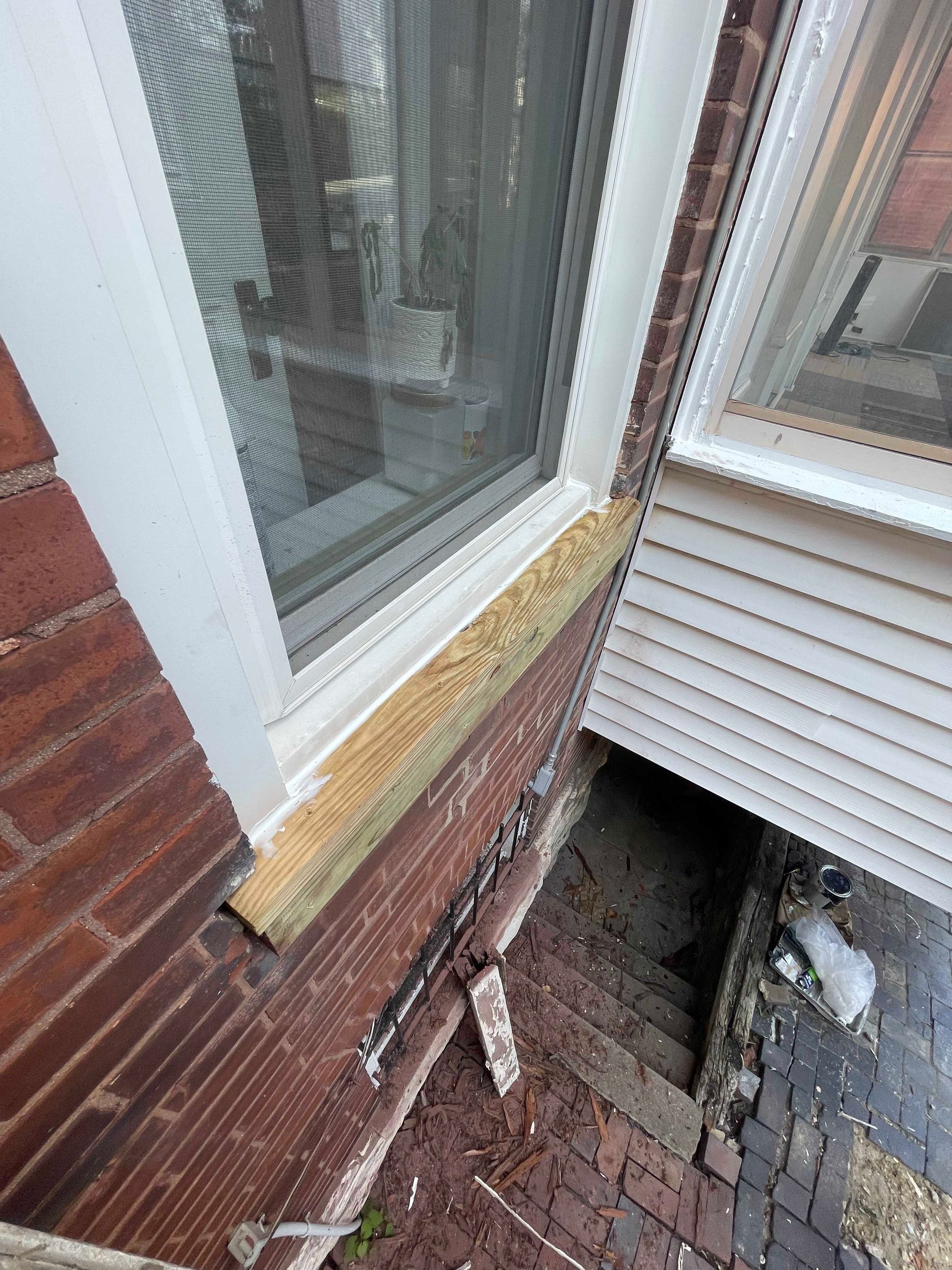 Exterior window with exposed wood trim against brick and siding.