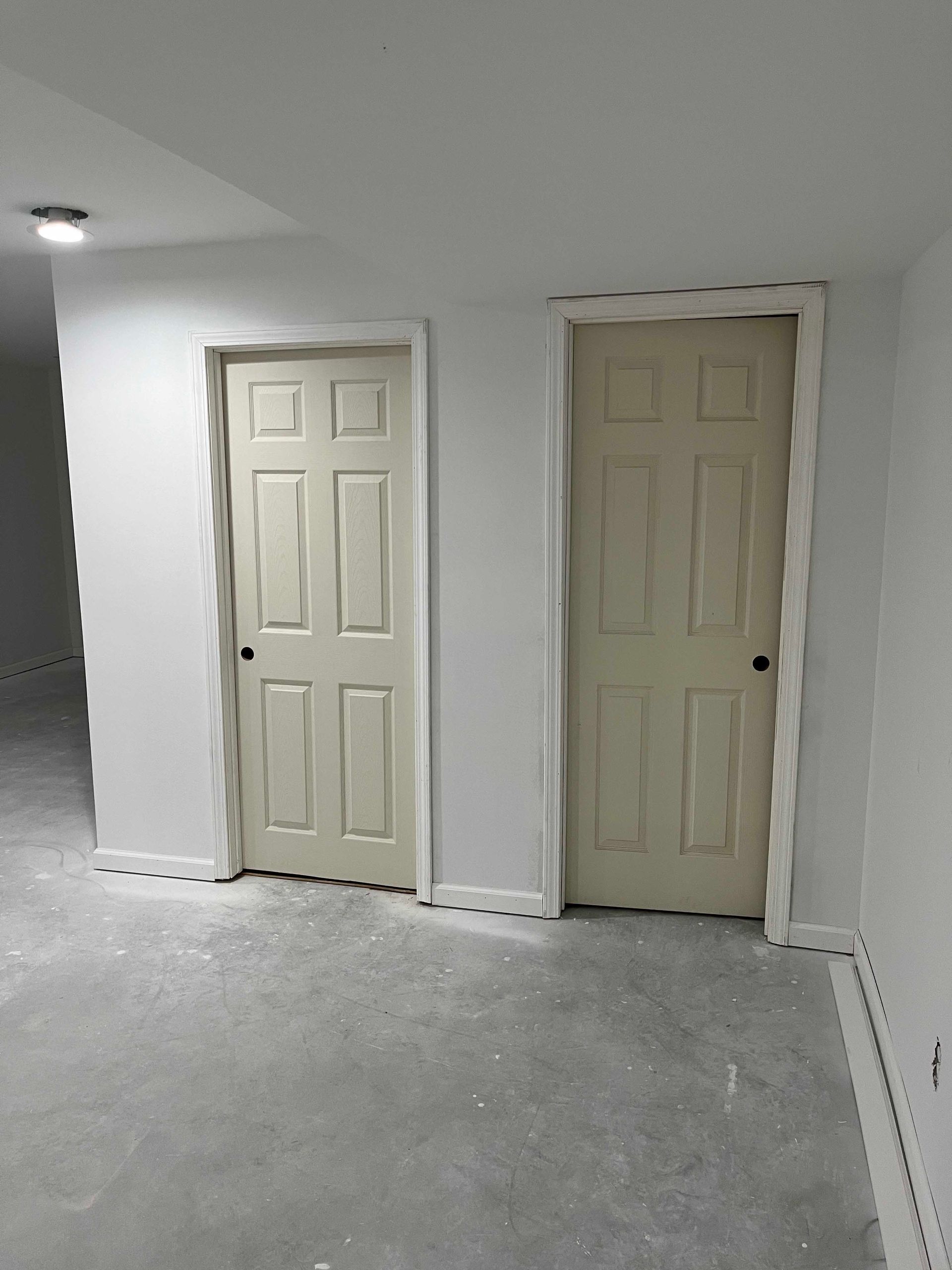 Two cream-colored doors in a room with light-gray walls and a concrete floor.