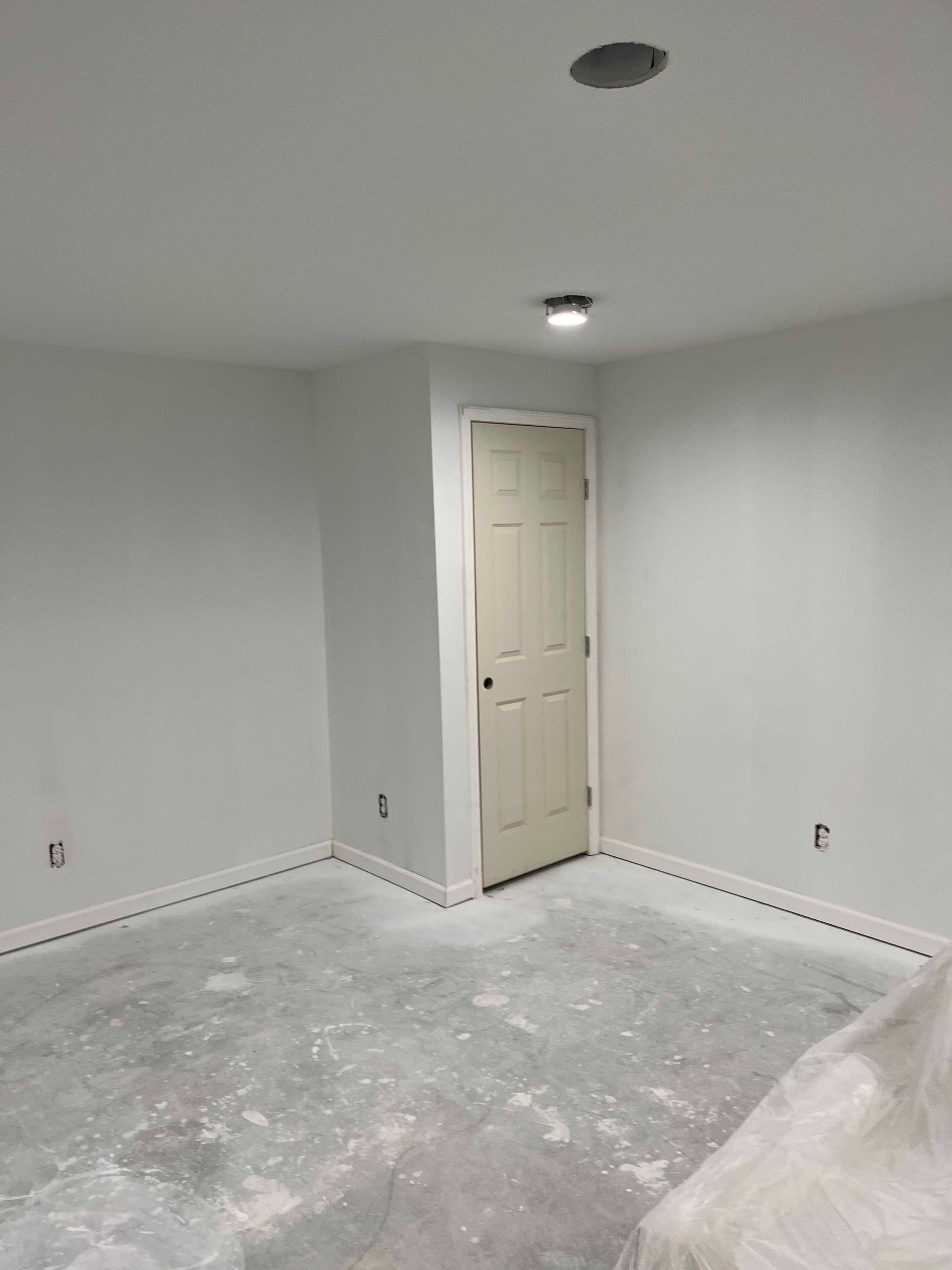 Empty room with white walls, a closed door, and a concrete floor.