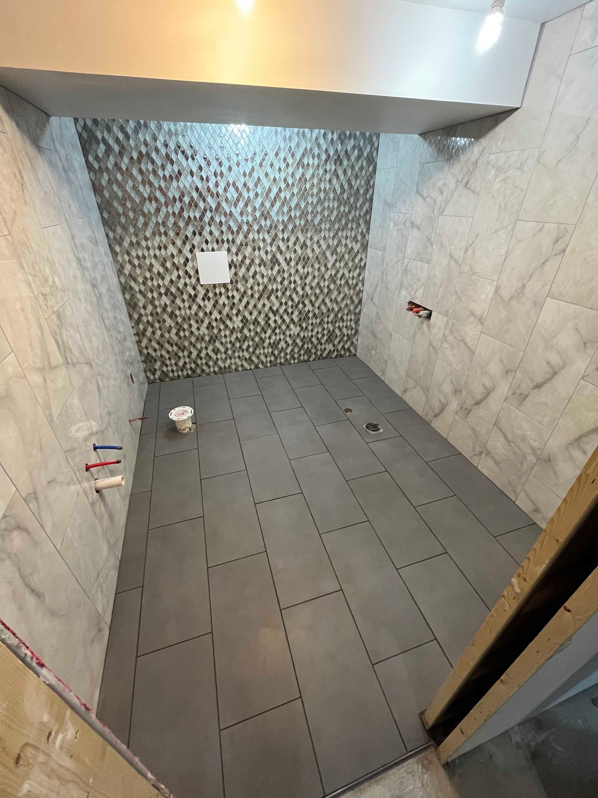 Bathroom under construction, gray tile flooring and walls, textured accent wall.