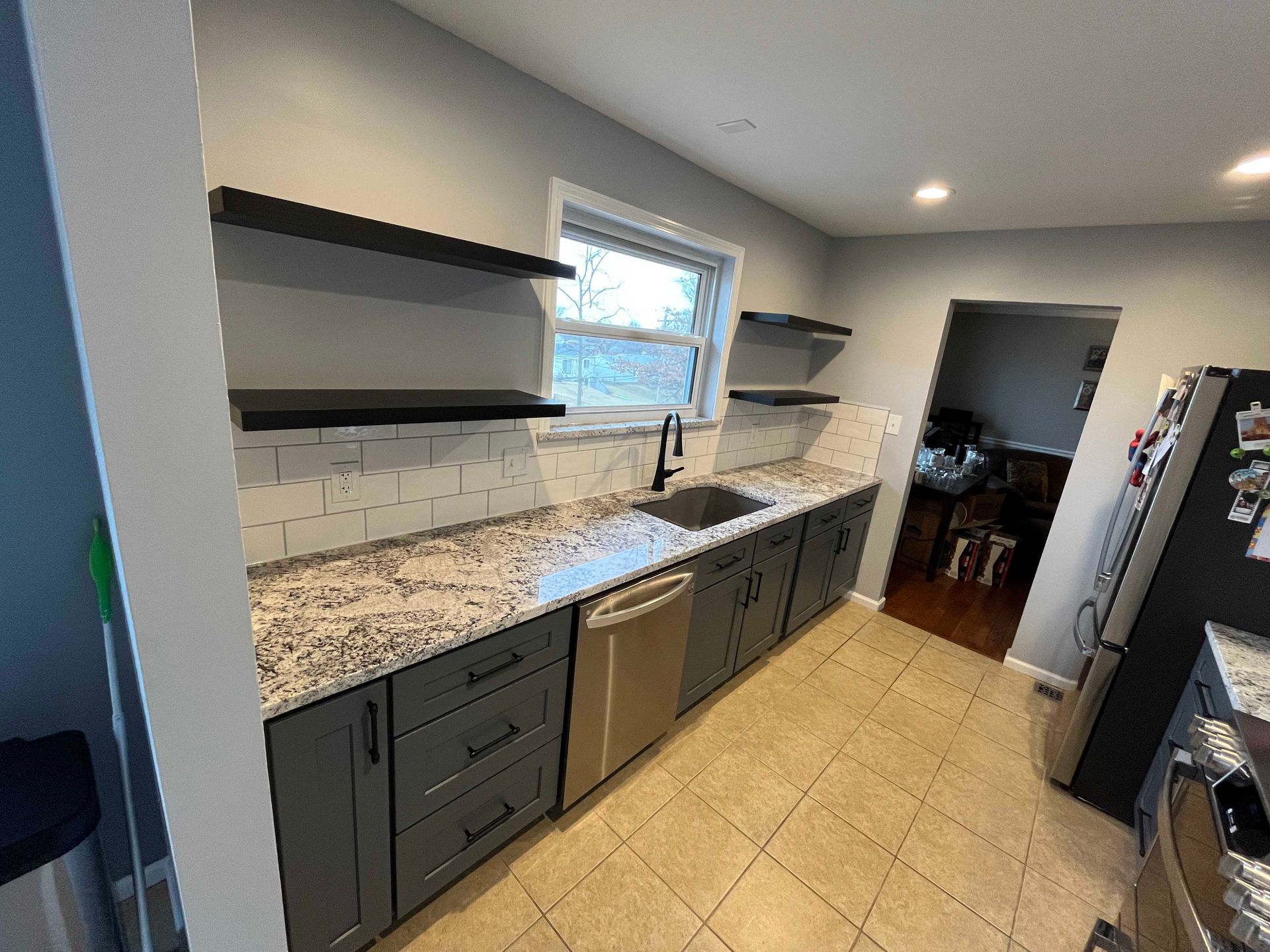 Gray kitchen with granite countertops, stainless steel appliances, open shelving, and a sink.