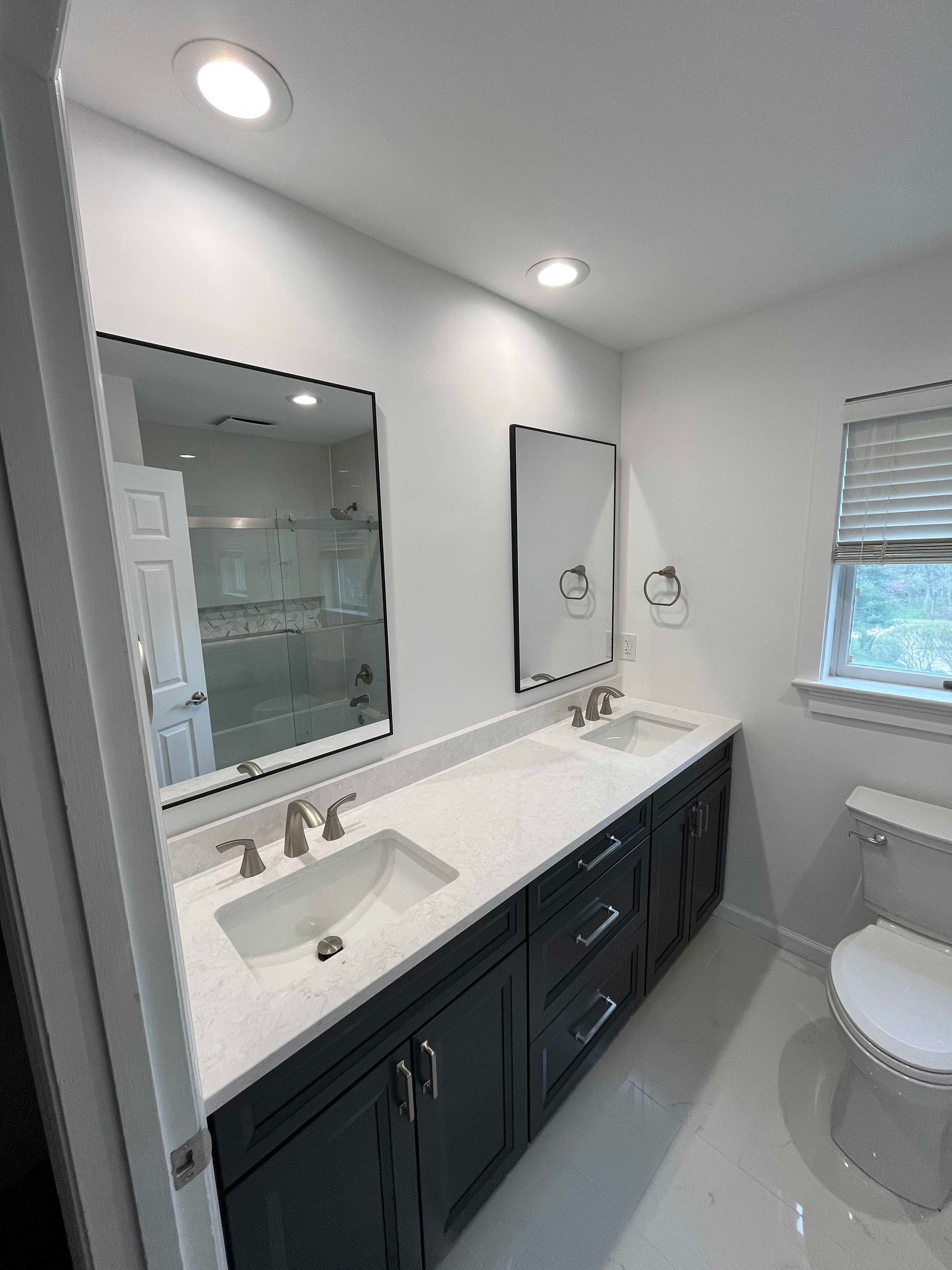 Bathroom with navy vanity, white countertop, two sinks, mirrors, and a toilet.
