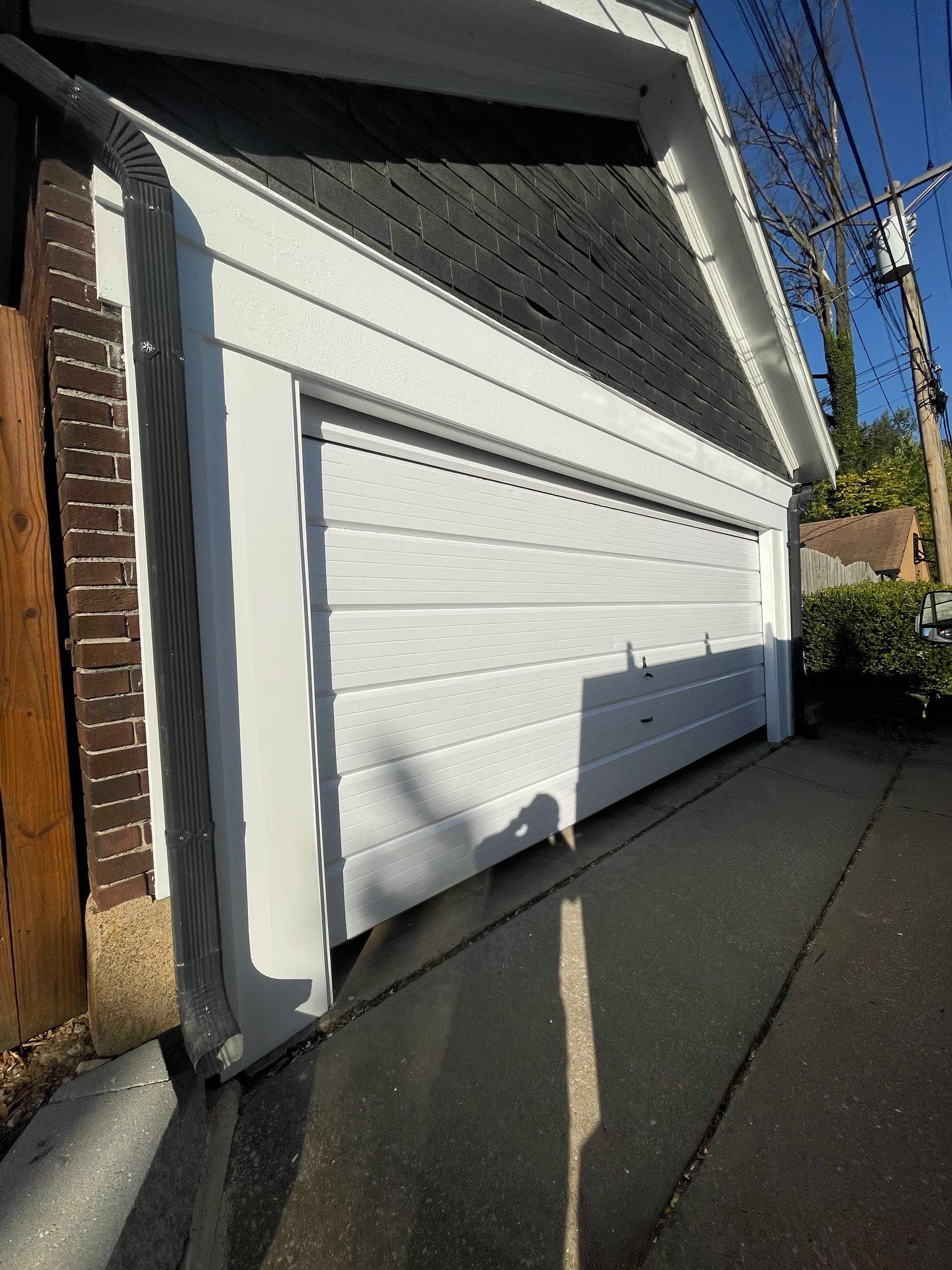 White garage door with white trim, gray siding, and a dark roof.