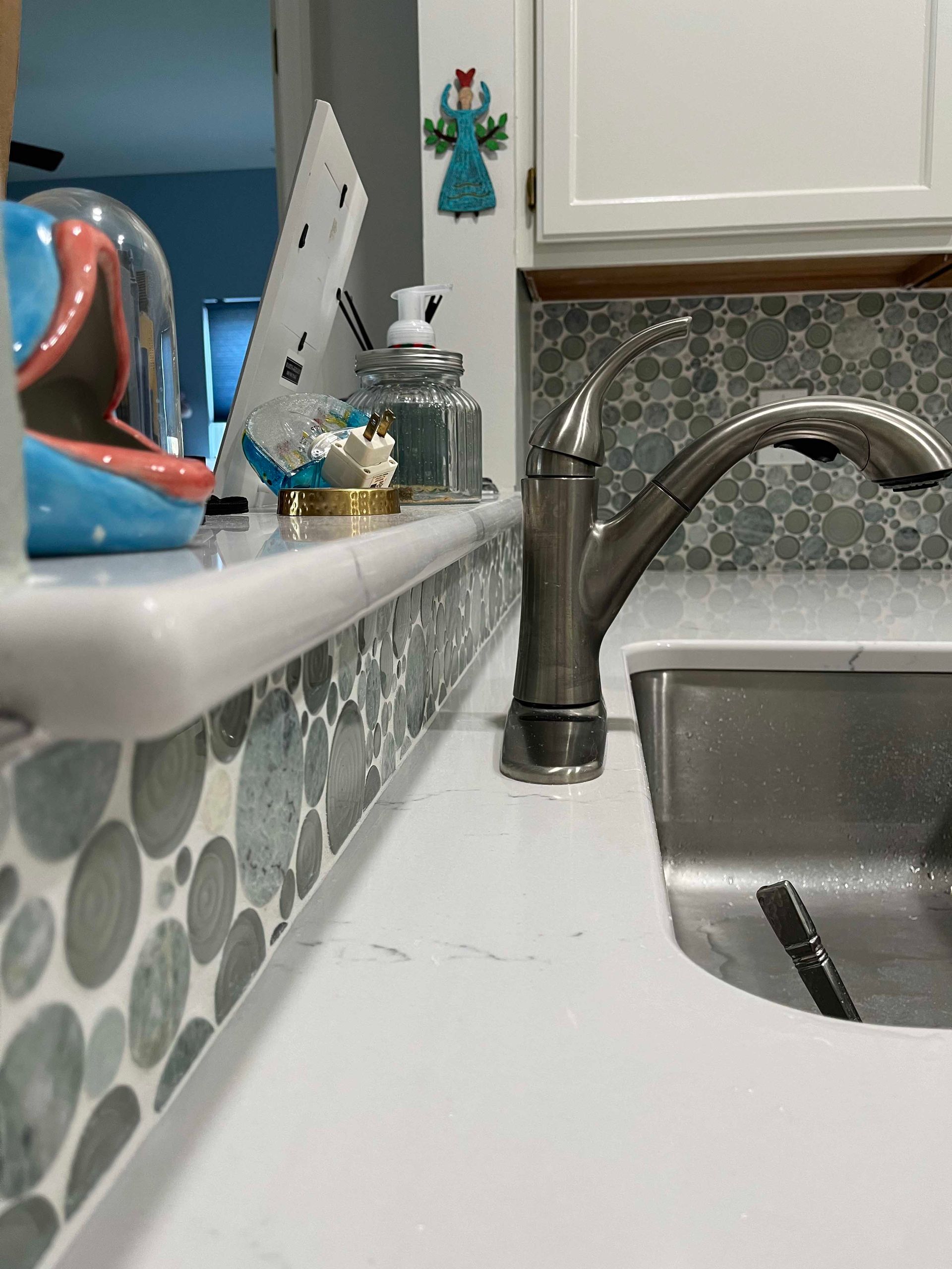 Kitchen sink with faucet, white countertop, and gray mosaic tile backsplash.