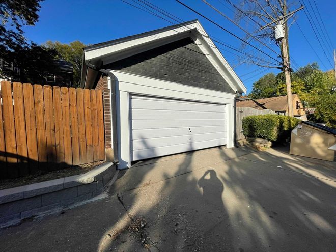 White garage with black roof, bordered by white trim and a wooden fence, on a sunny day.