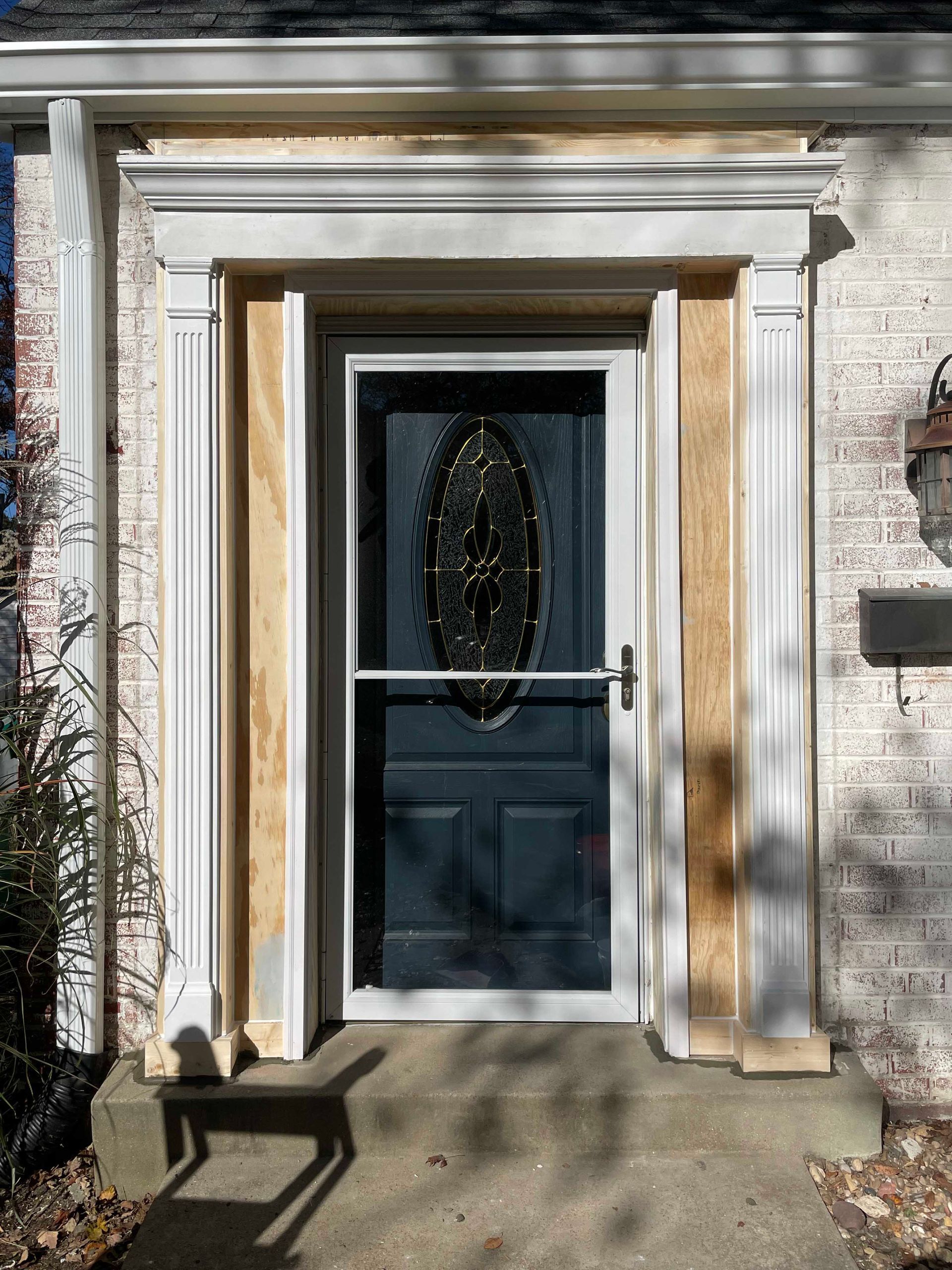 Front door framed with white molding and a storm door. Dark blue door with oval glass.