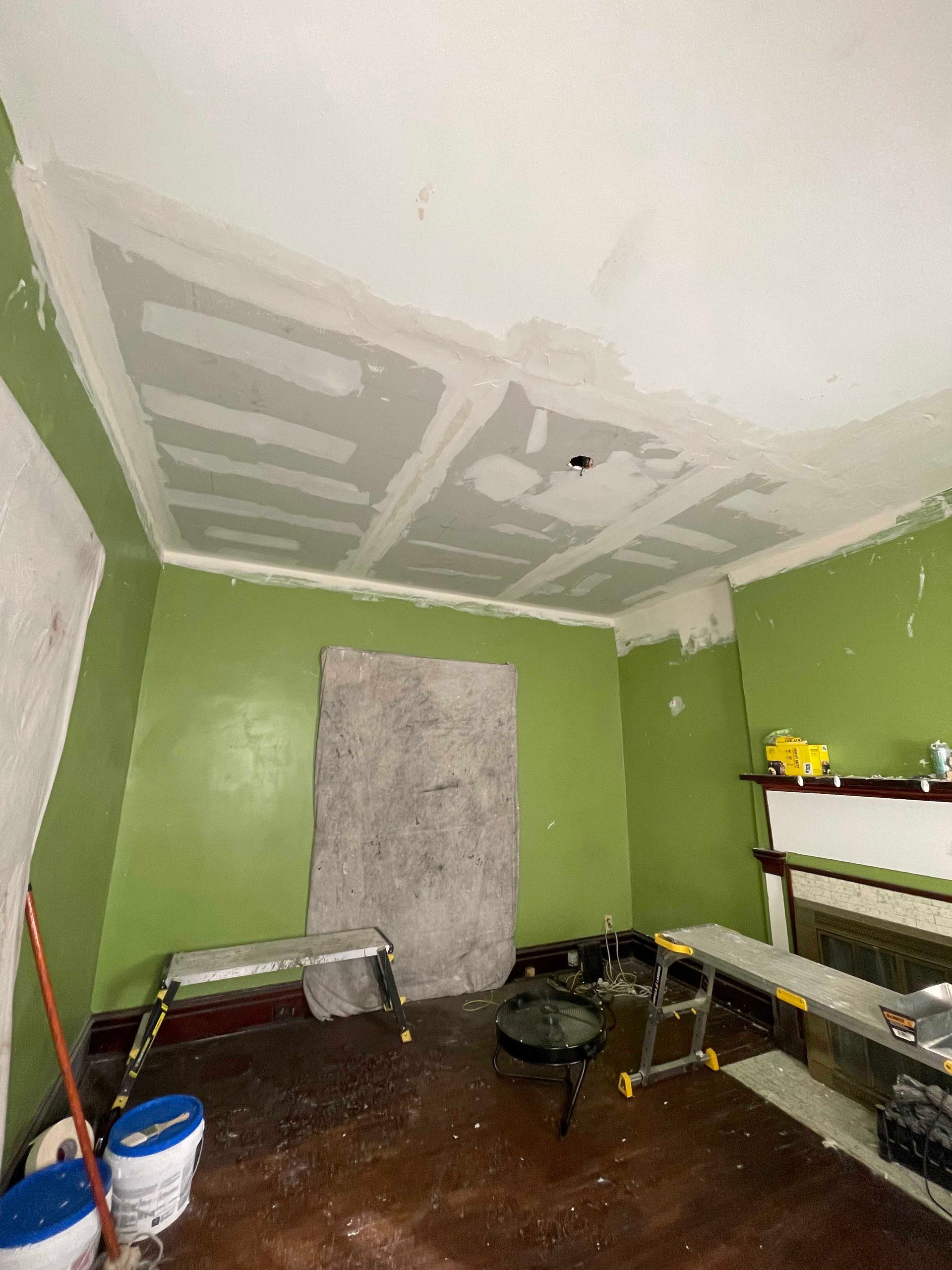 Room under renovation with green walls, partially finished ceiling, and dark wood floor.