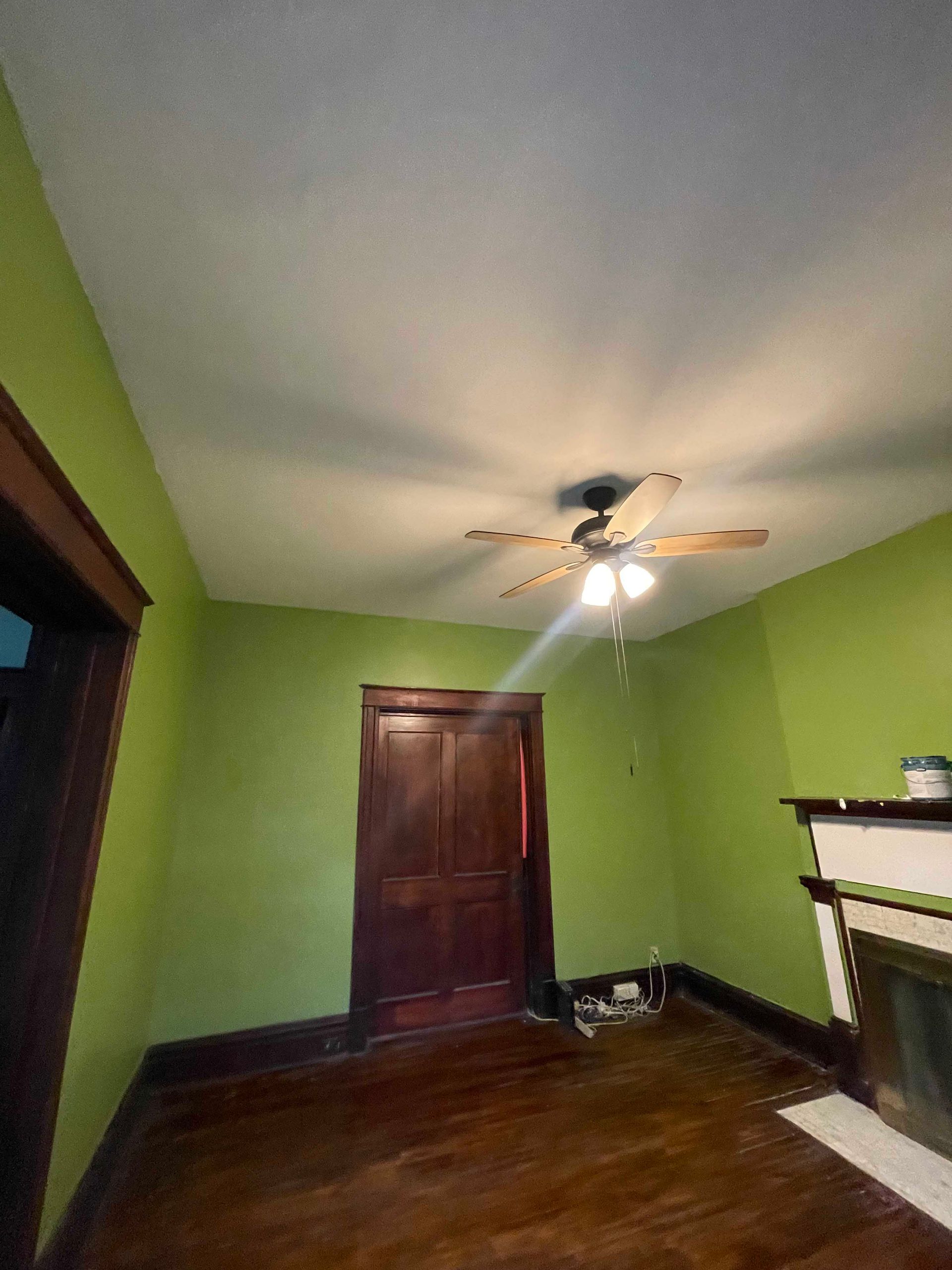 Room with green walls, brown door, dark wood floor, white ceiling, and a ceiling fan.