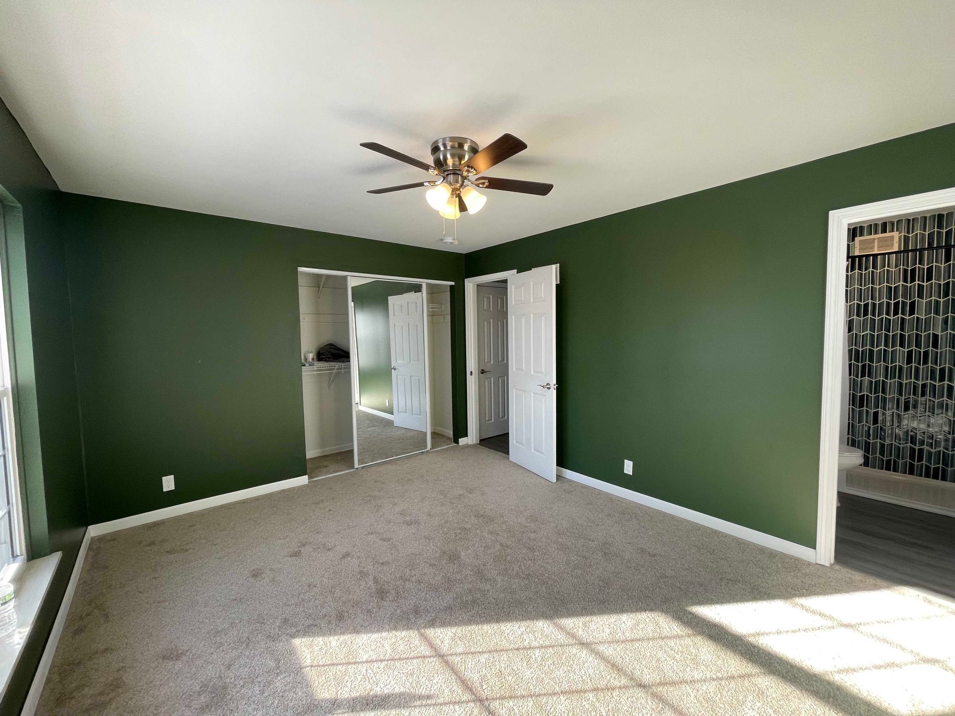 Empty room with green walls, white doors, and beige carpet. Sunlight streams through a window.