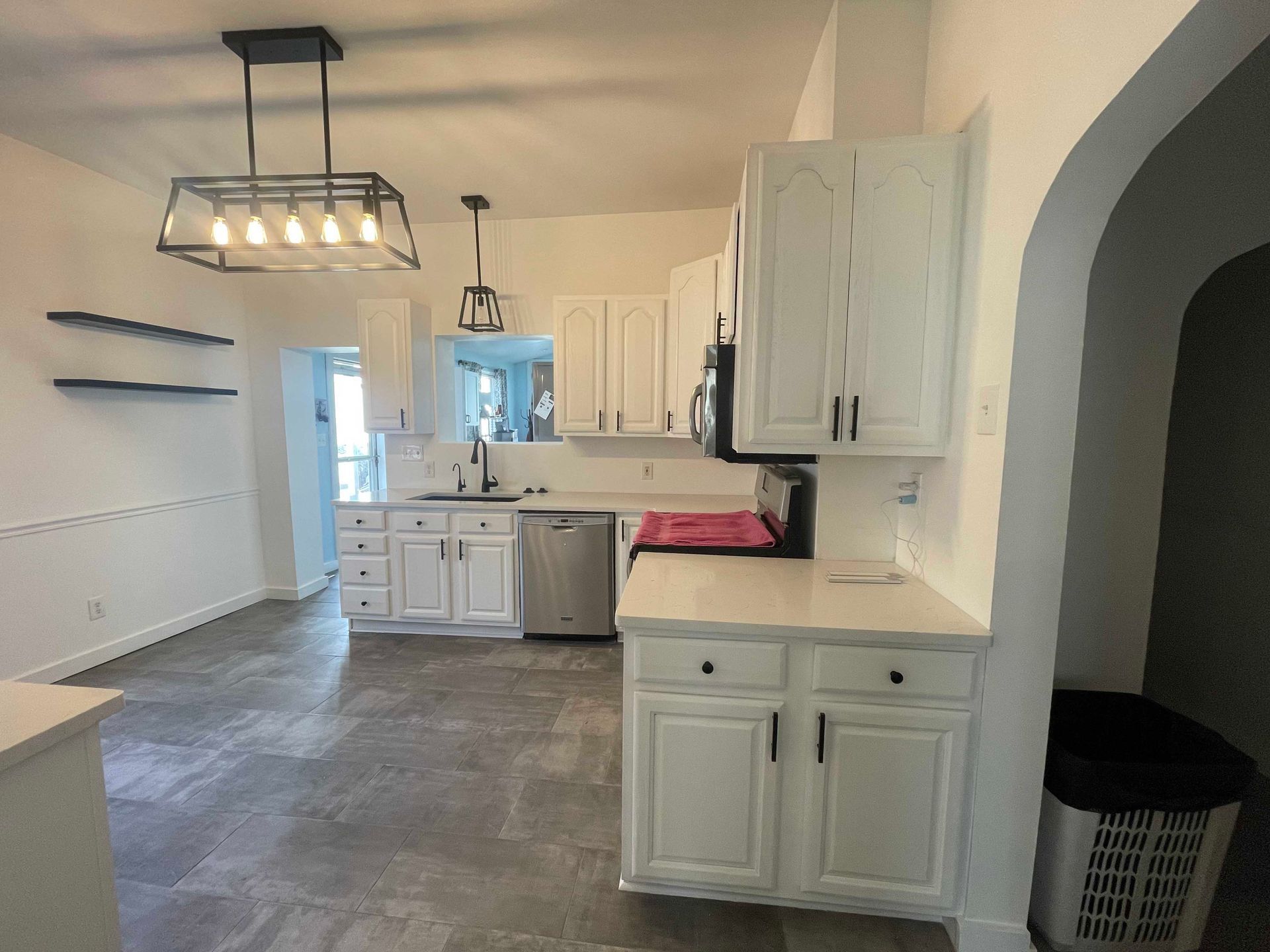 White kitchen with cabinets, stainless steel appliances, and a hanging light fixture.