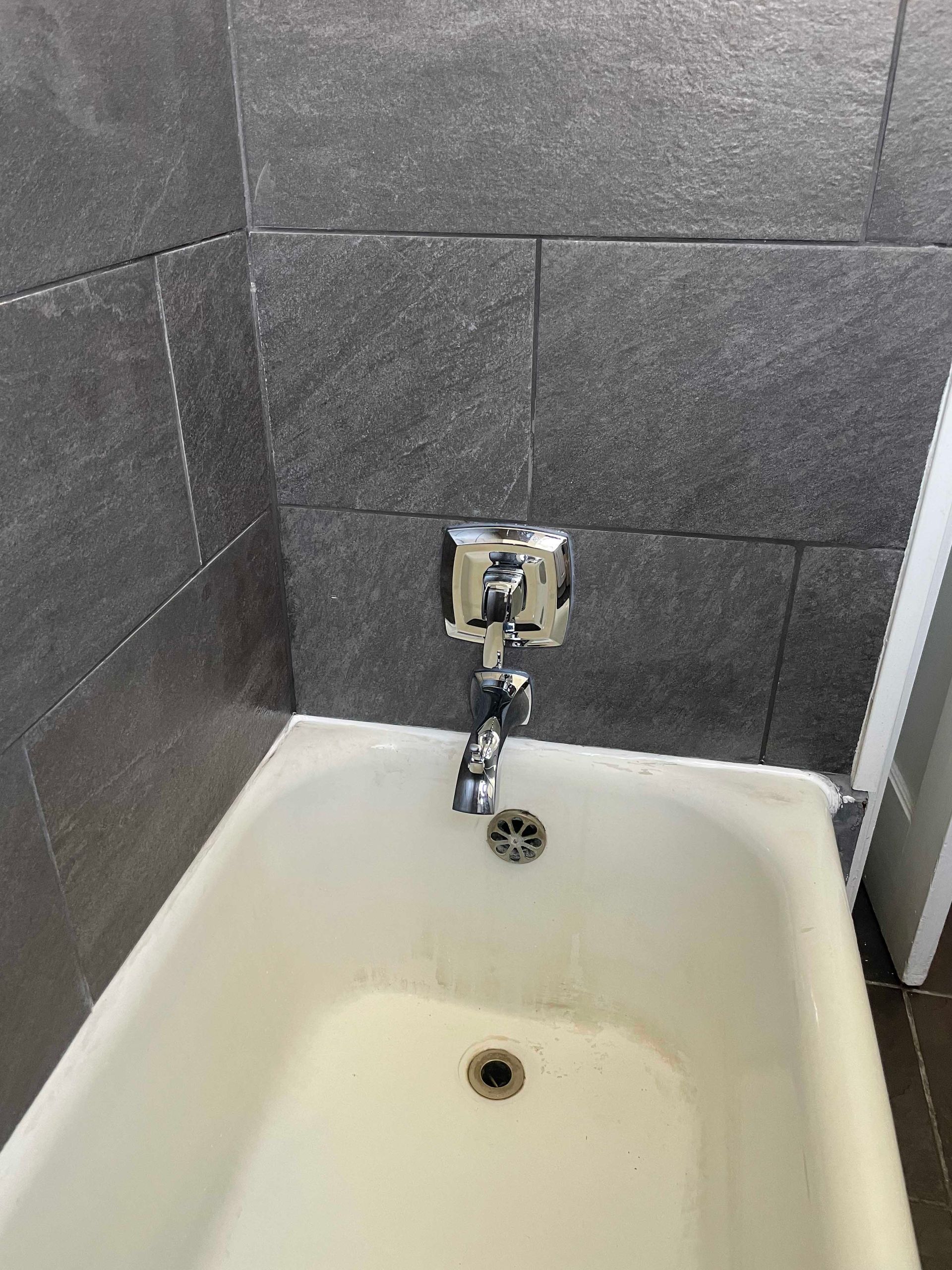 Bathtub with chrome faucet, drain, and dark gray tiled wall.