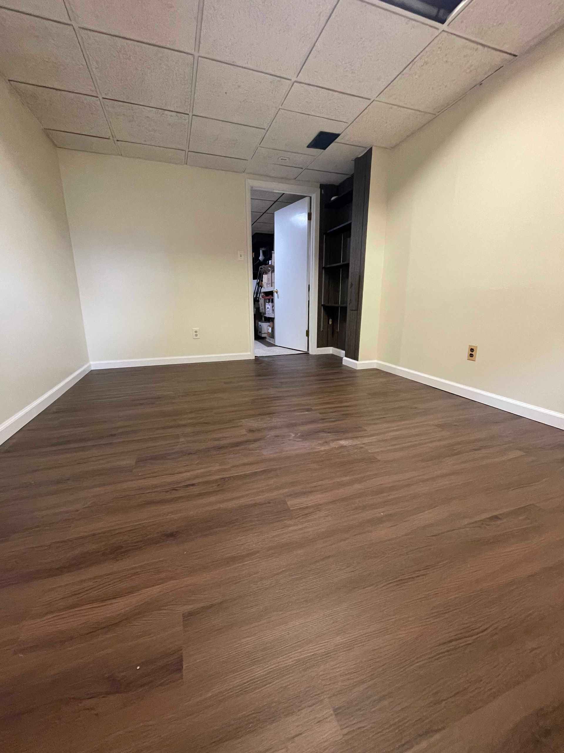 Empty room with dark wood-look flooring, beige walls, and a white ceiling with a door in the back.