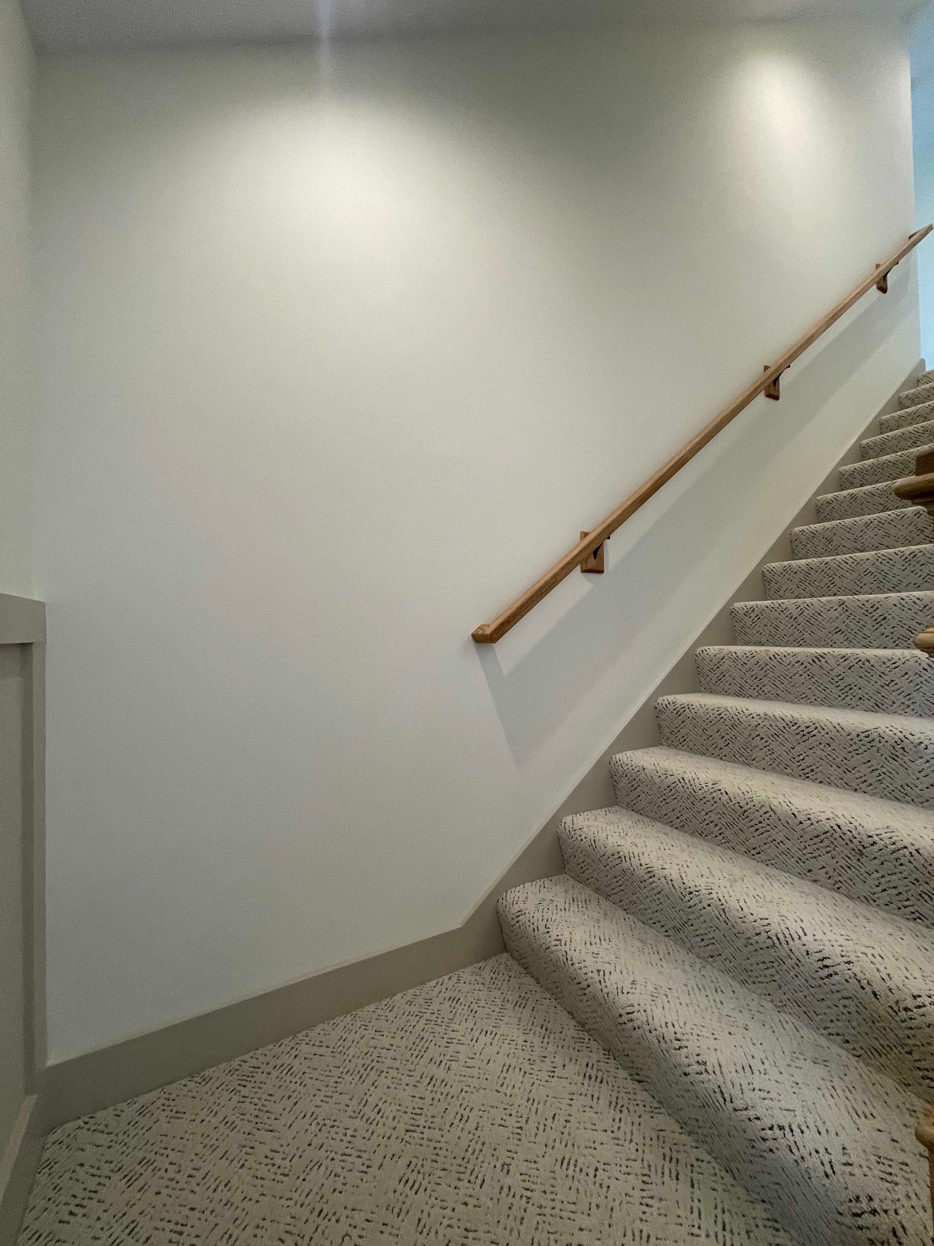 Staircase with terrazzo steps and a wooden handrail against a white wall.