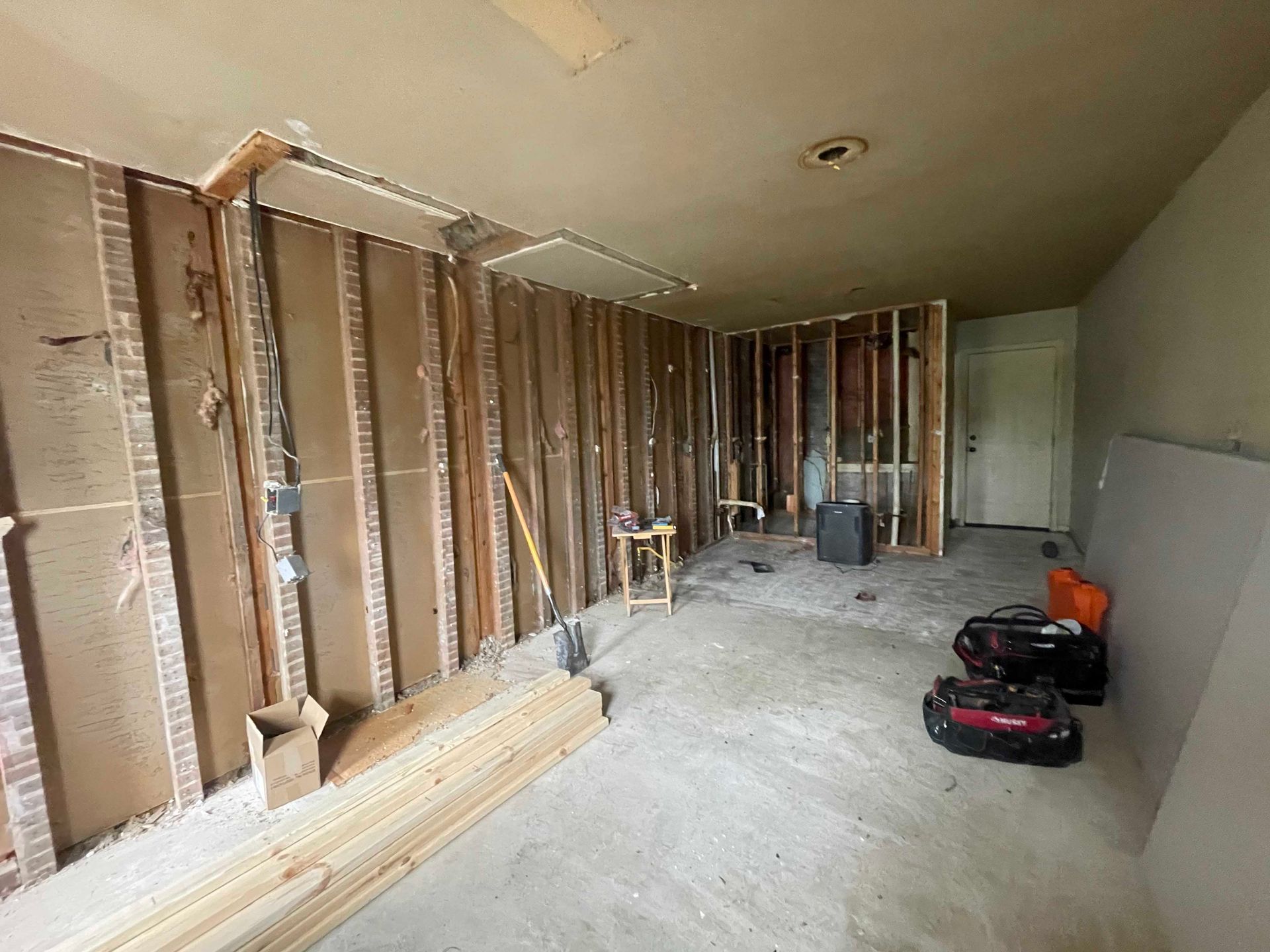 Interior room gutted for renovation. Exposed wooden studs and brick, concrete floor, tools visible.