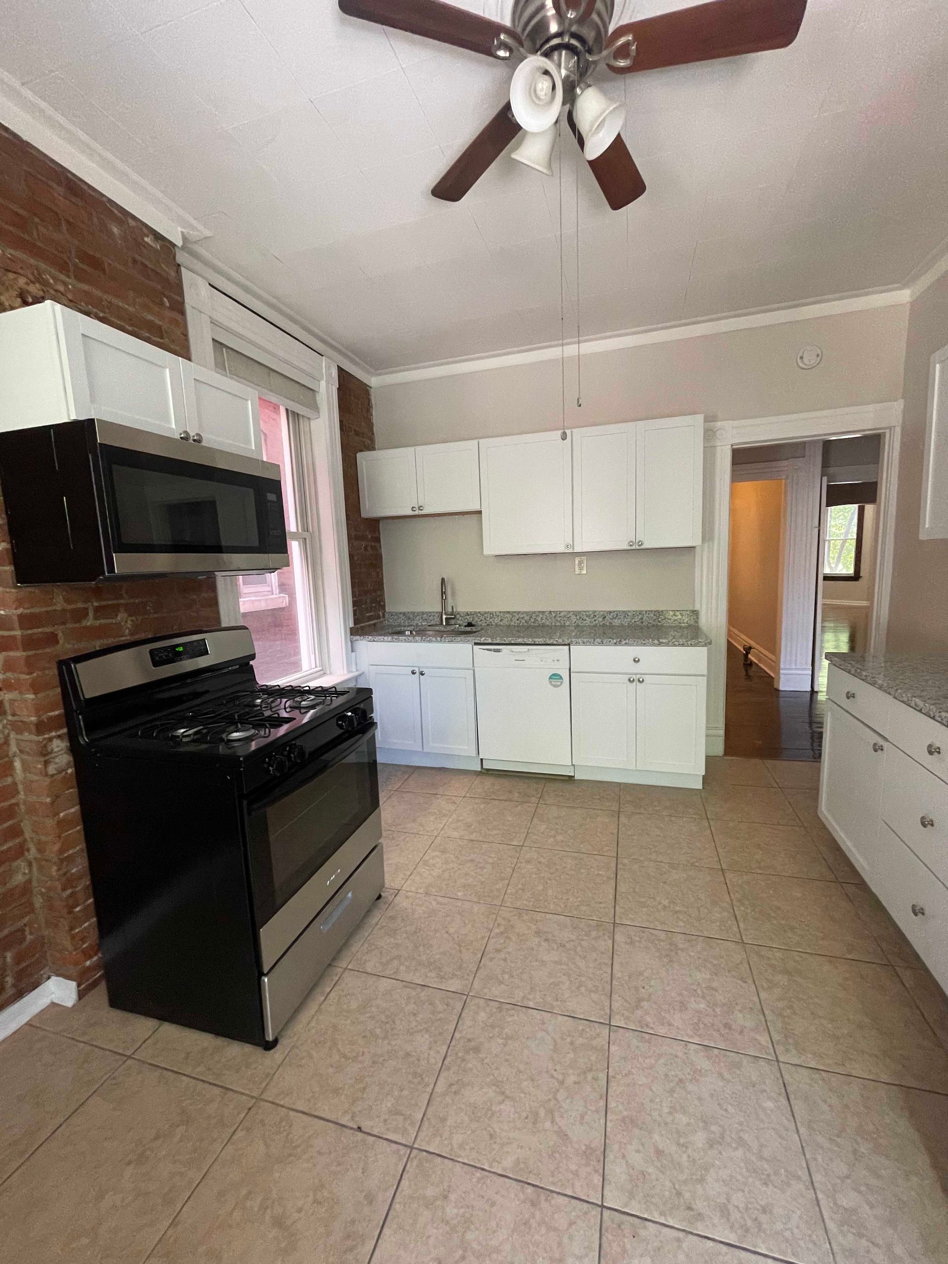 Kitchen with white cabinets, stainless steel appliances, brick wall, tile floor.