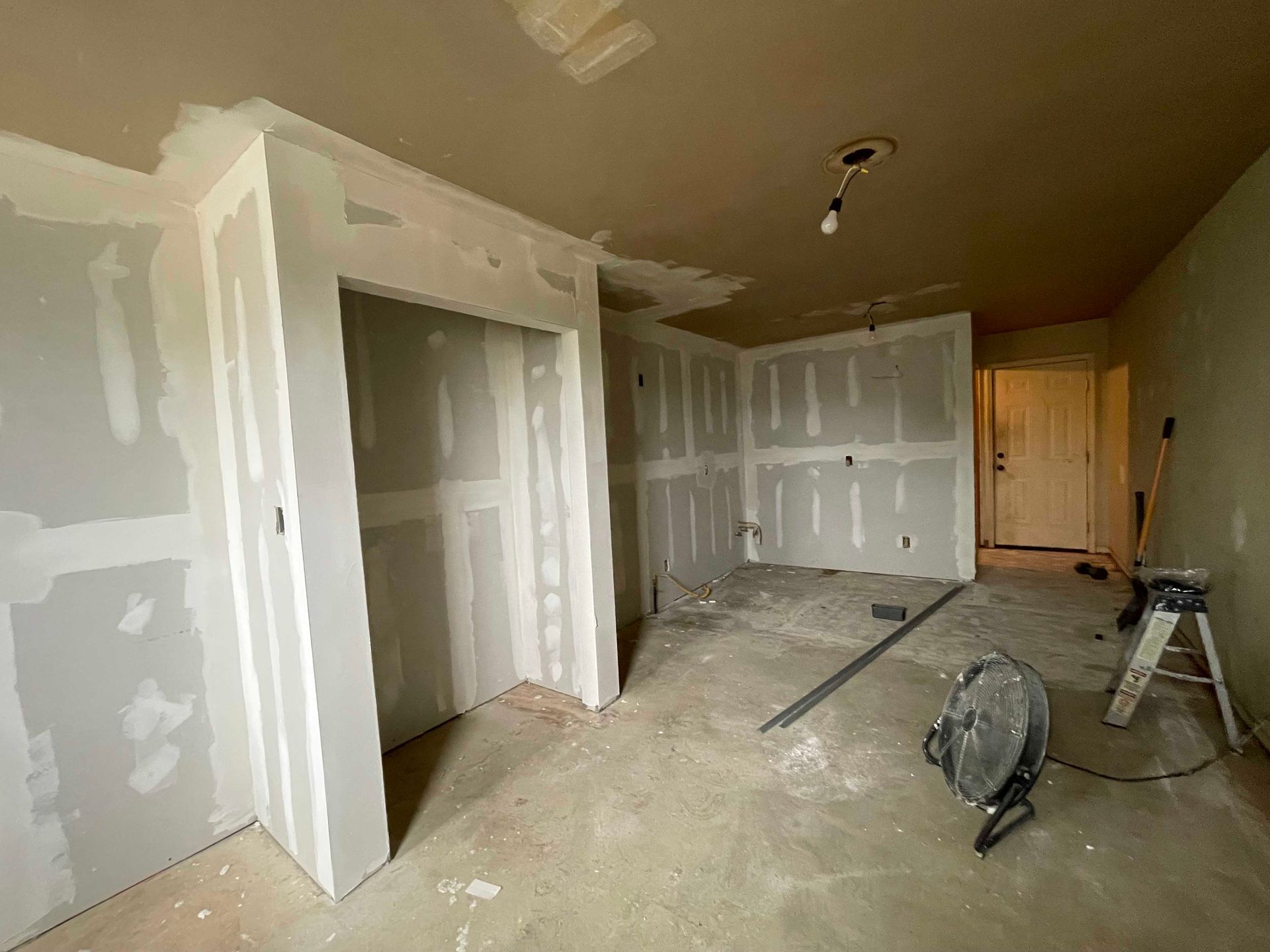 Room under construction with drywall installed.  Gray walls, cement floor, closet doorway, and tools.