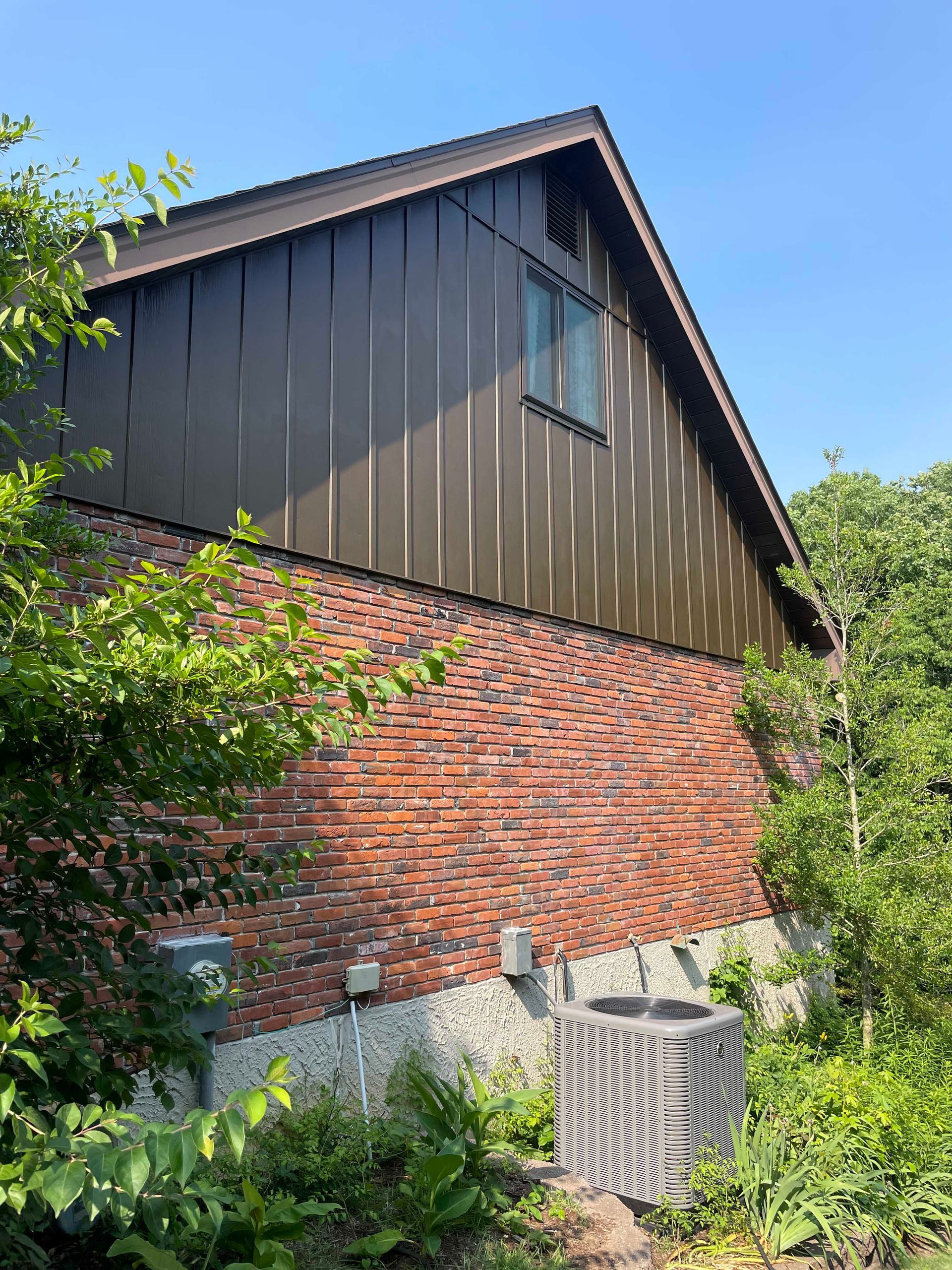 Brick building with brown metal siding and a window, surrounded by green trees.