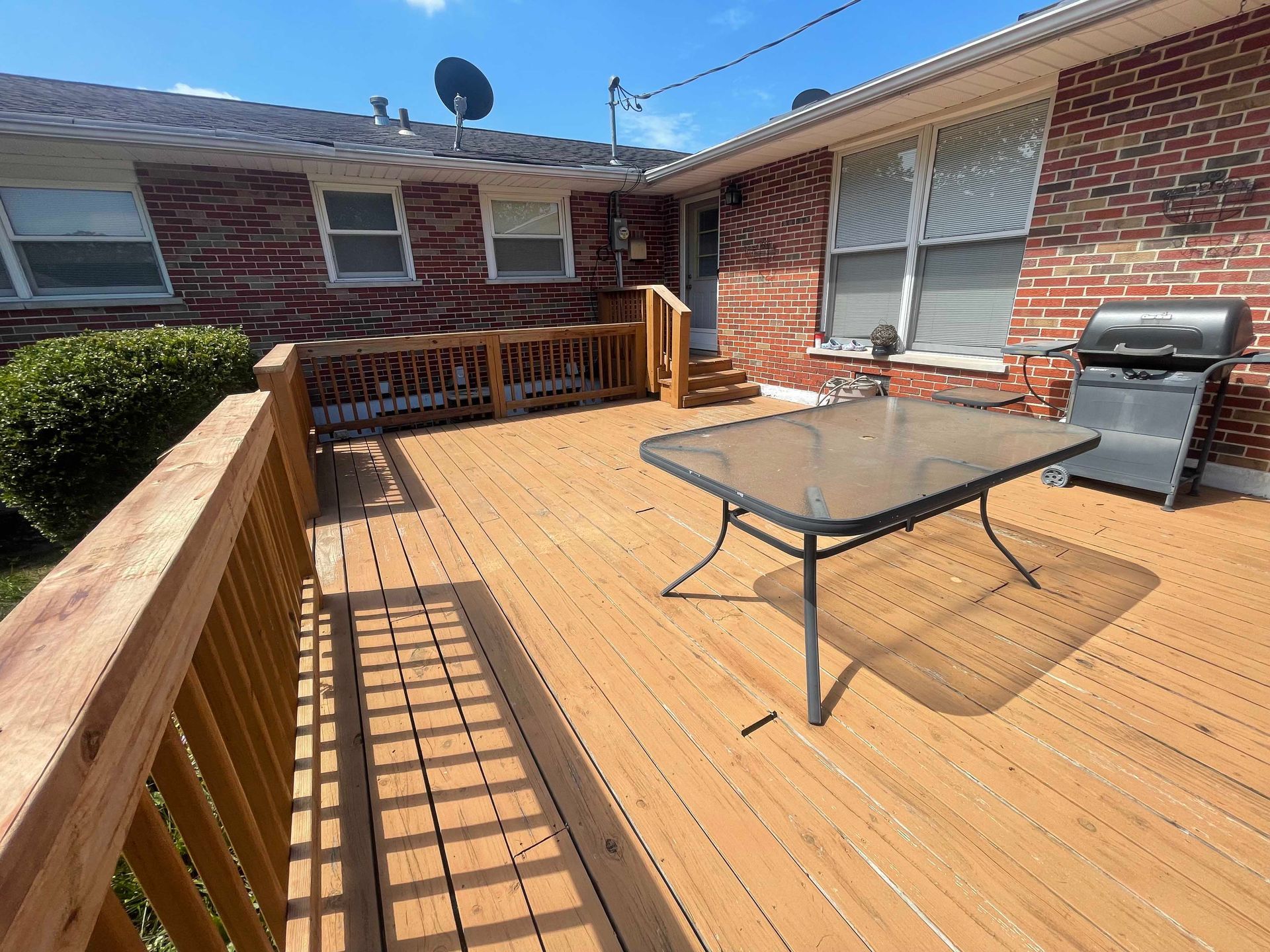 Wooden deck with table and grill against brick building.