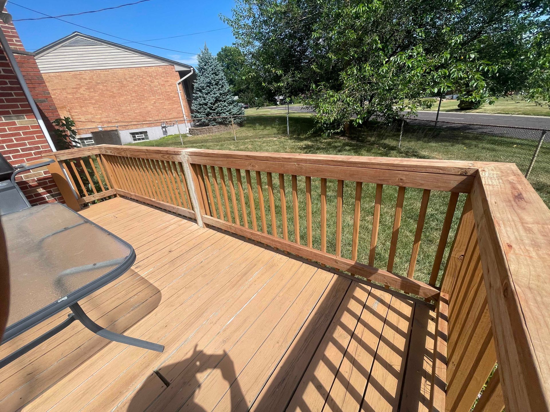 Wooden deck with railing, brown wood, and a table outdoors in a sunny setting.