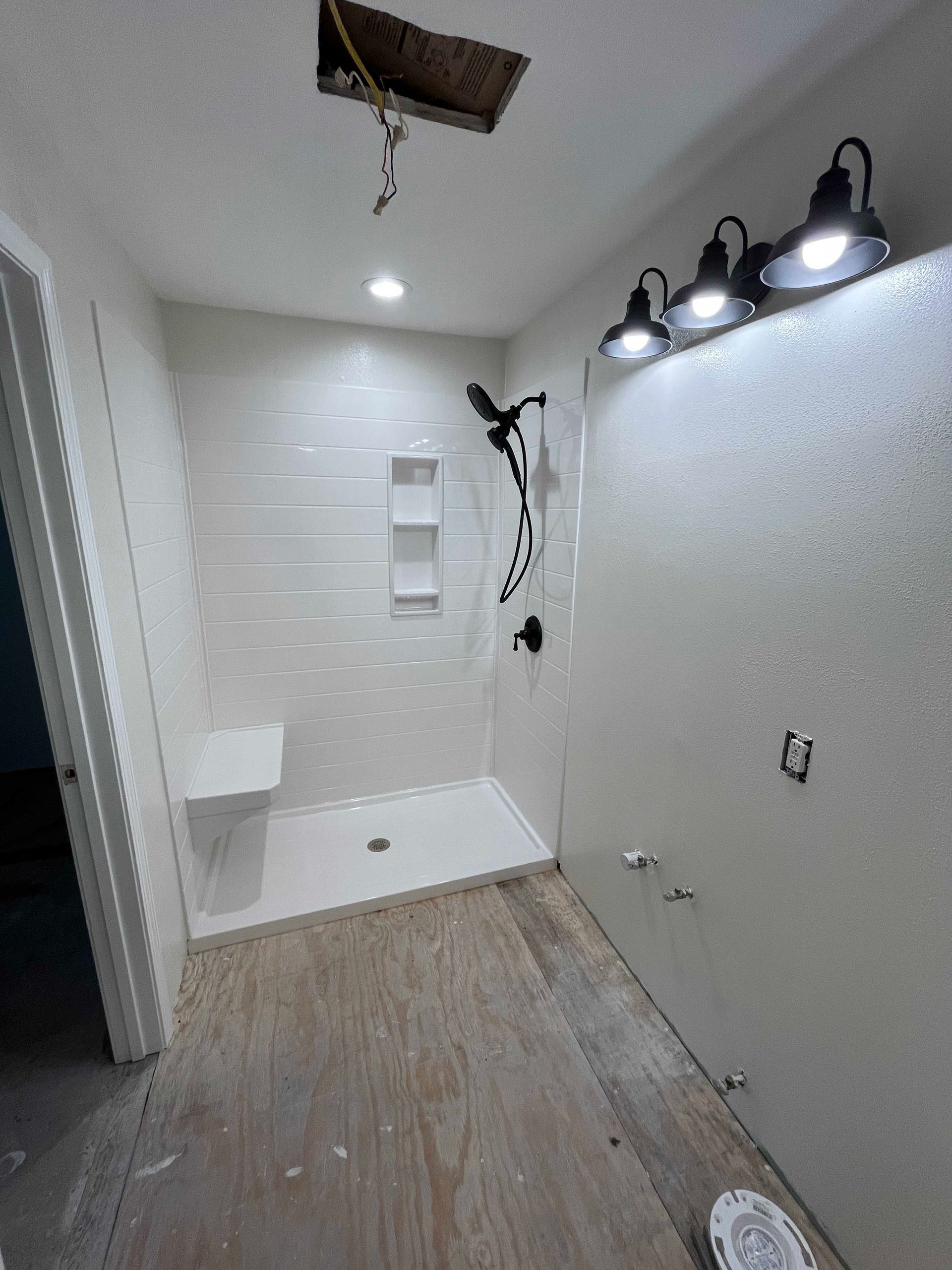 Bathroom remodel, white tiled shower with seat, black fixtures, and three overhead lights.