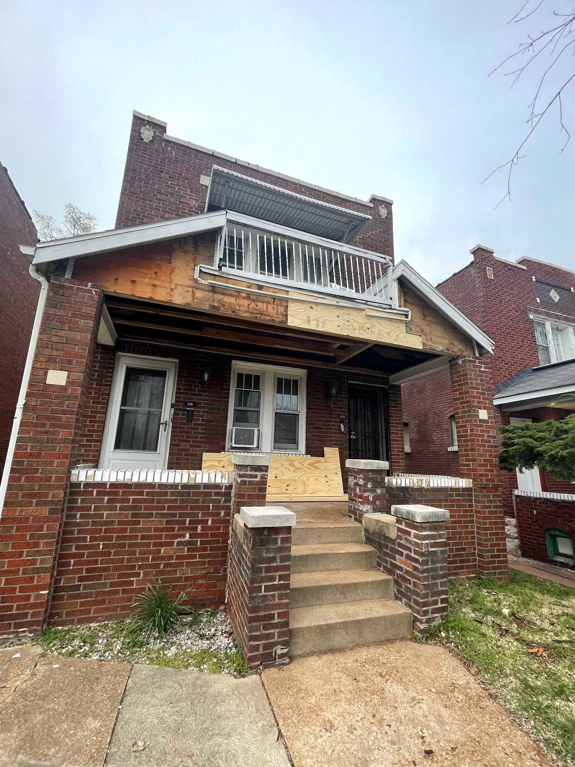 Two-story brick house, partial wood facade, balcony with icicles, front steps leading to entrance, cloudy sky.