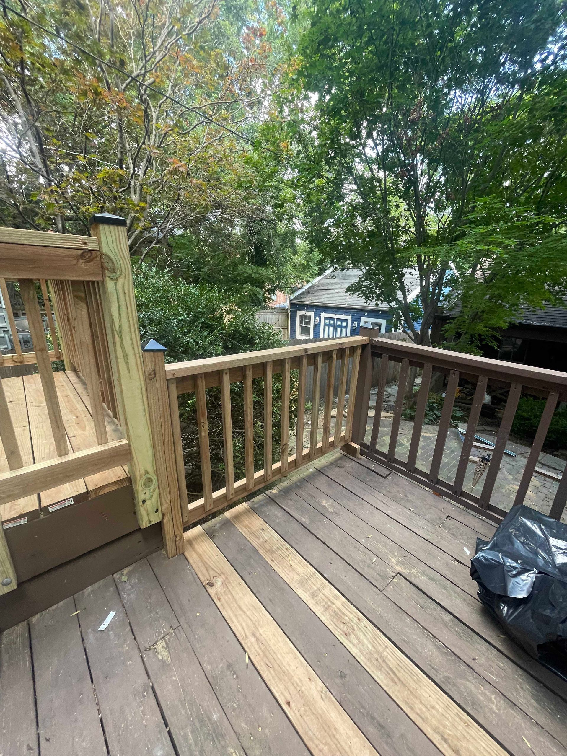 Wooden deck with railing, trees in background, partially shaded, sunny.