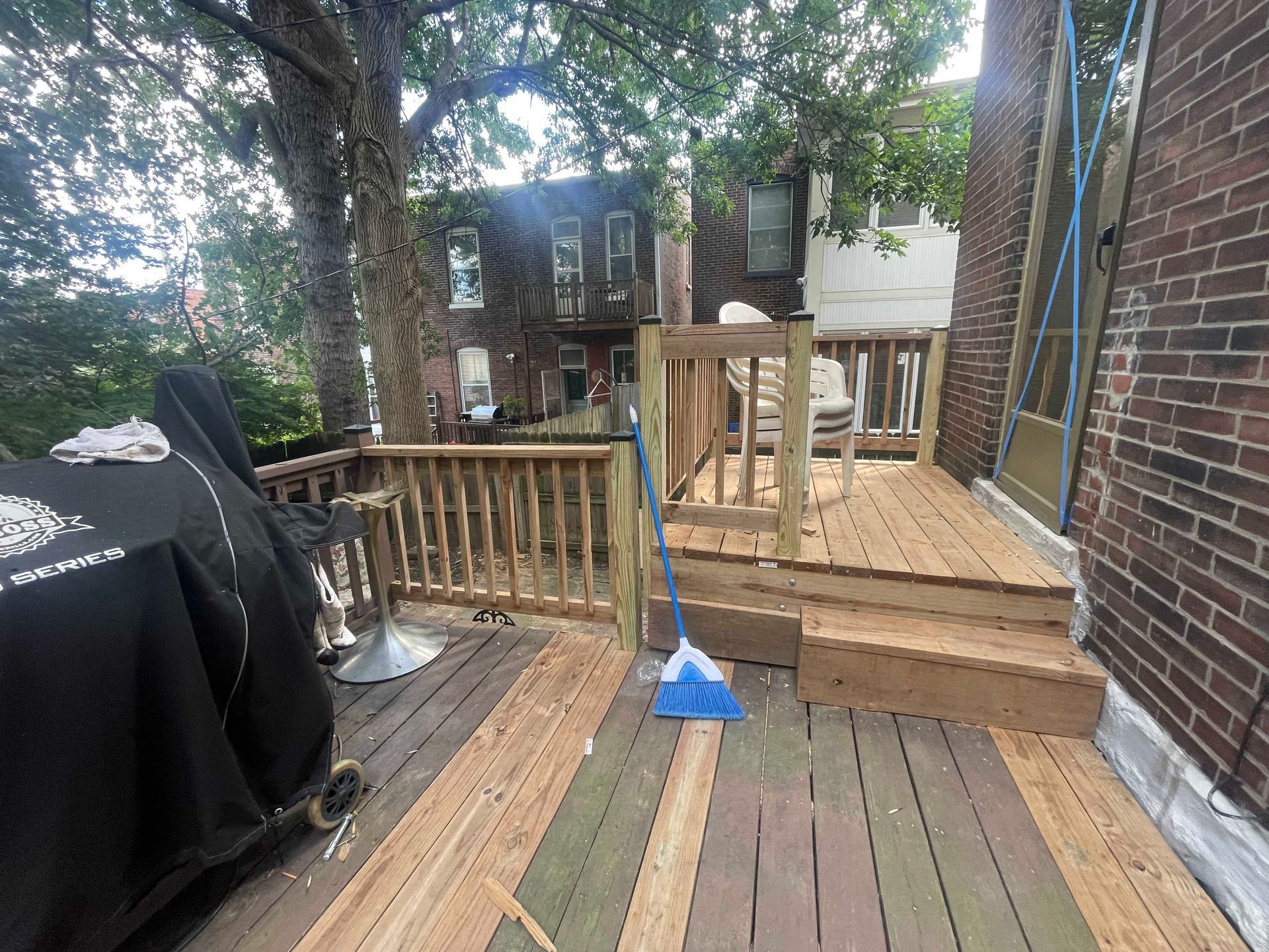 Wooden deck with railings and steps, connected to a brick building; a grill with a cover is present.