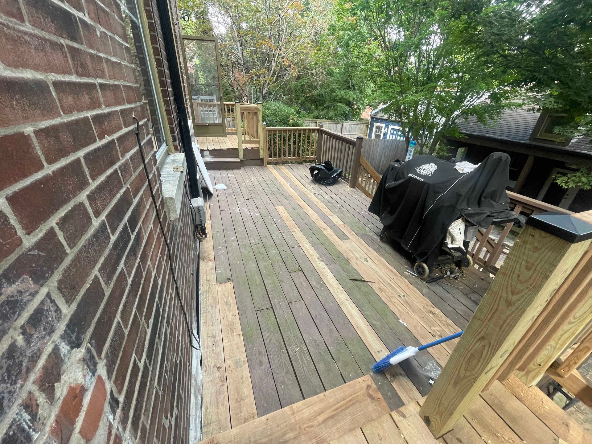 Wooden deck next to a brick building; partially covered grill and railing visible.
