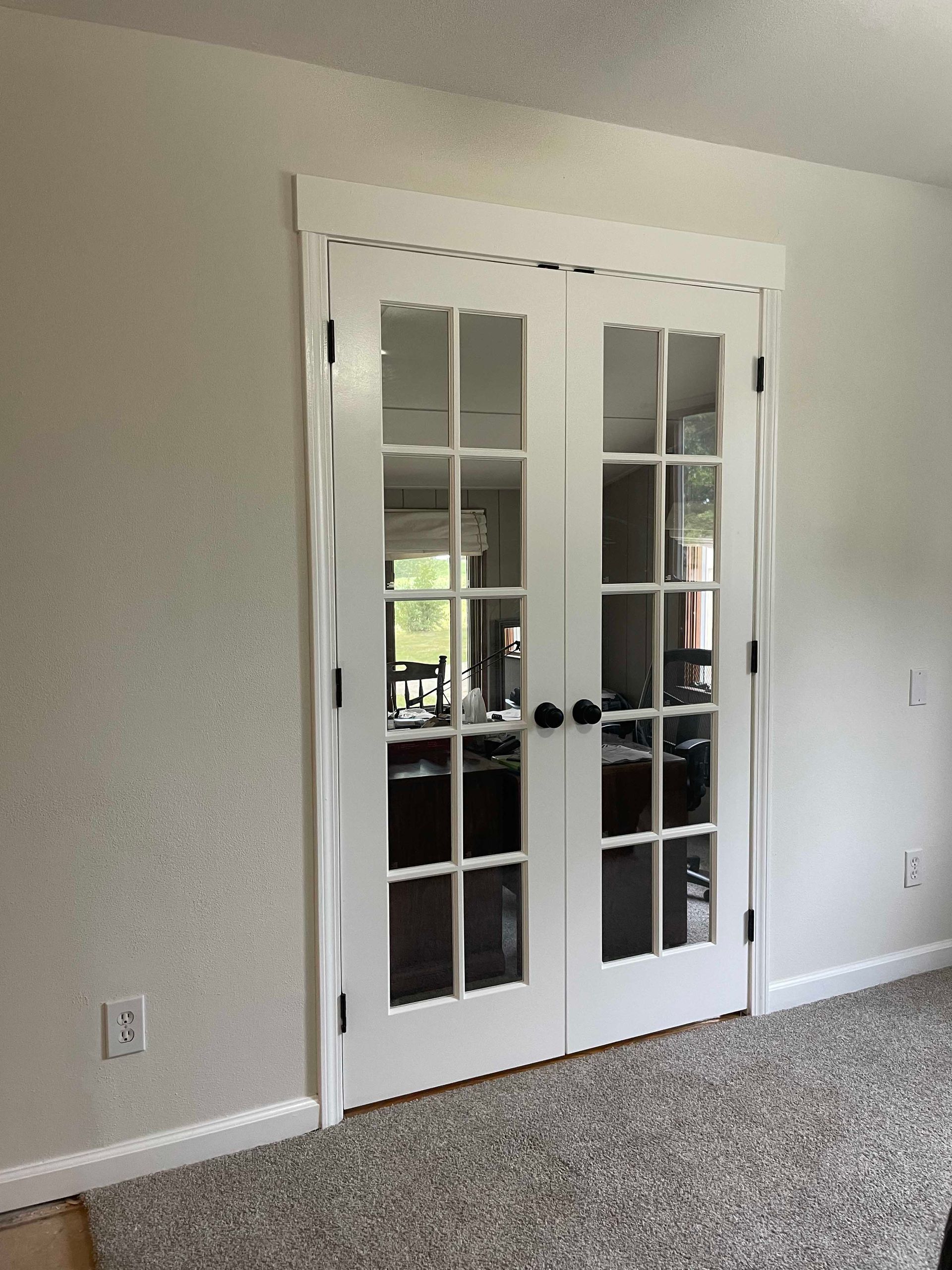 White French doors with multiple glass panes set in a white door frame on a light-colored wall.
