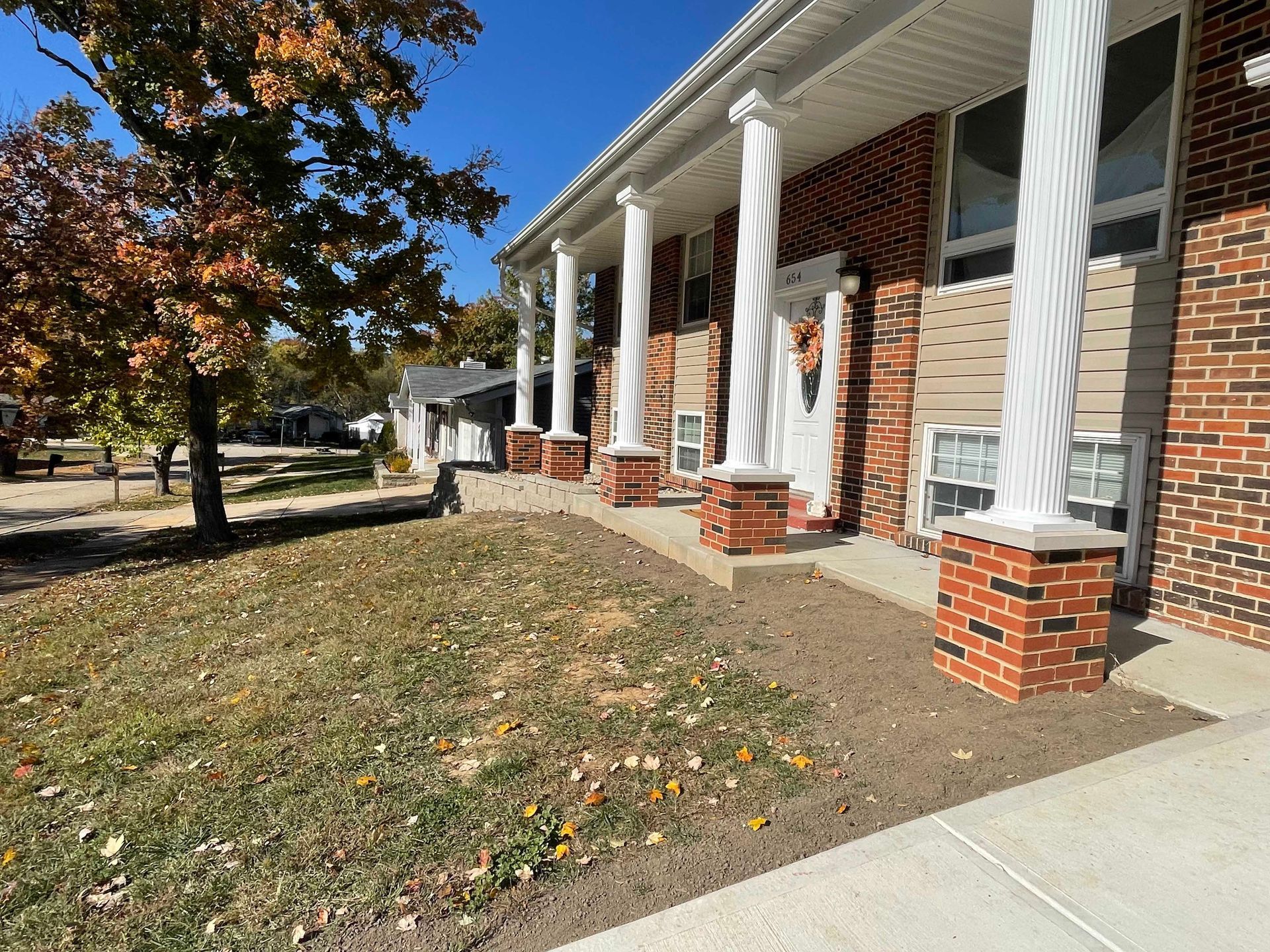 Brick building with white-covered columns, autumn trees, and a blue sky.