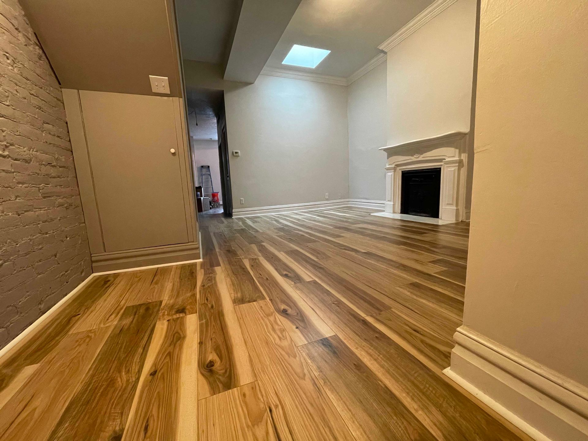 Hardwood-floored room with white fireplace and skylight. Light streams across the floor.