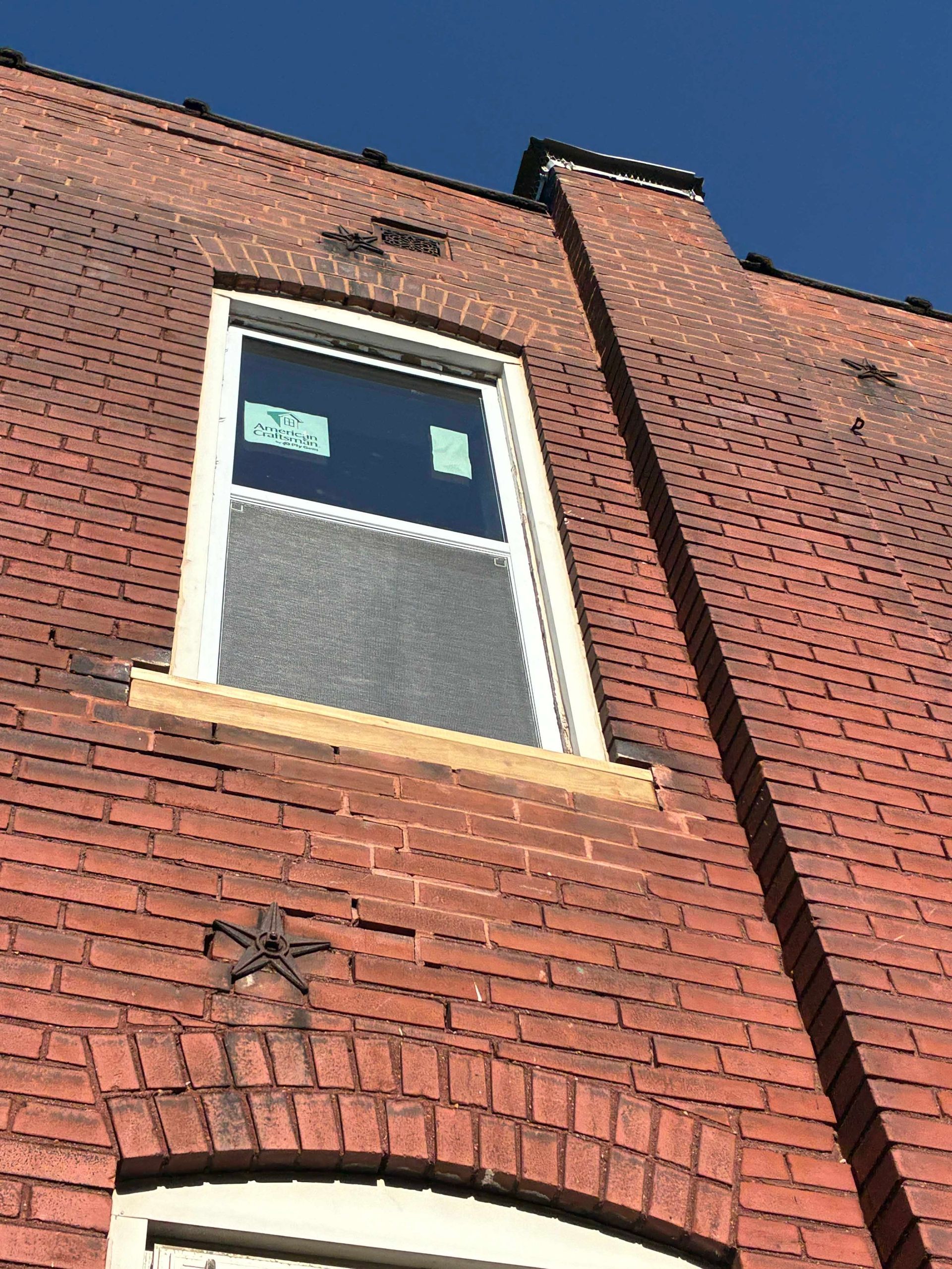 Brick building with a new window. Bright sky above.